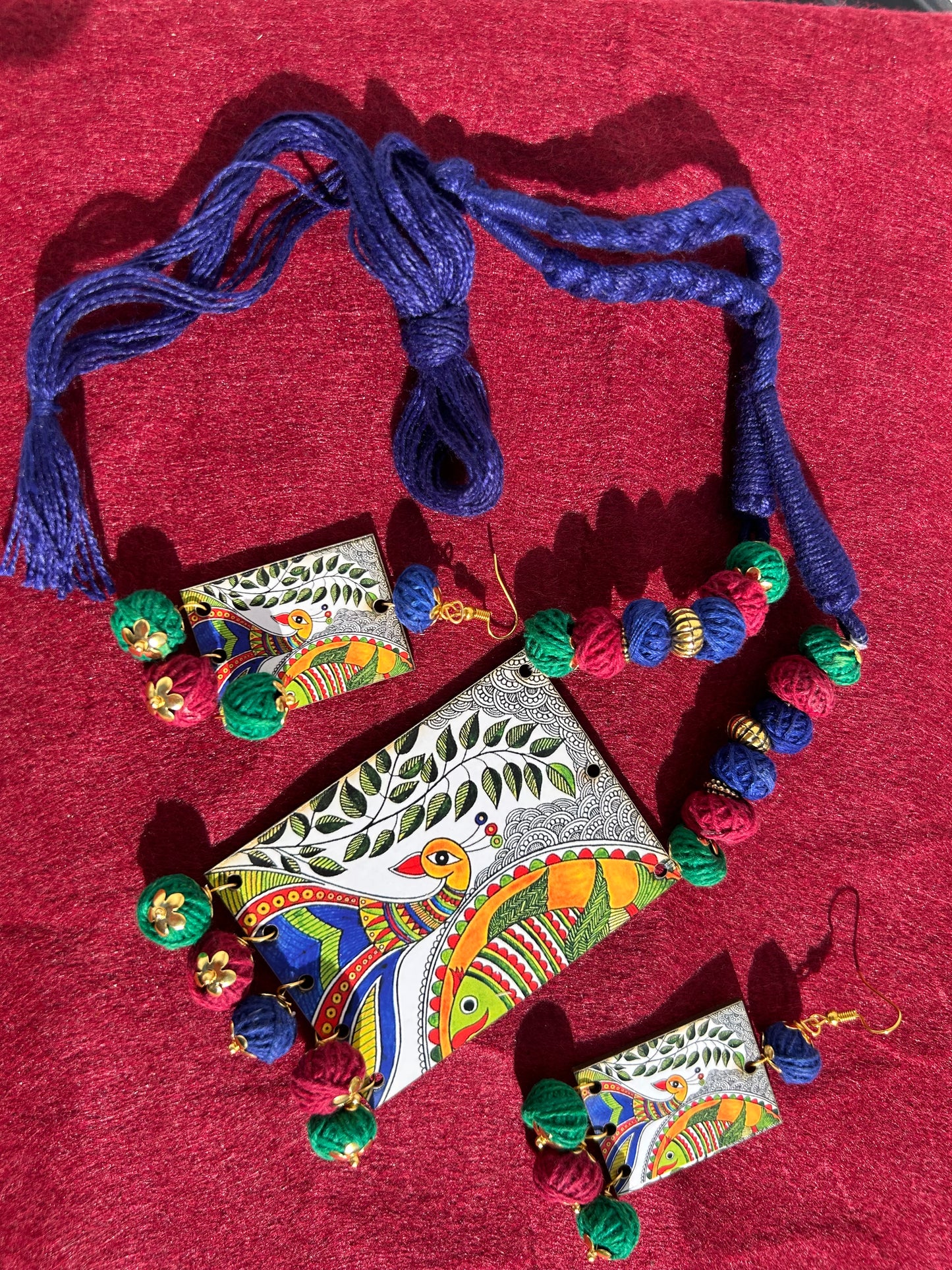Colorful decorative items including a necklace, earrings, and a pendant on a red fabric background.