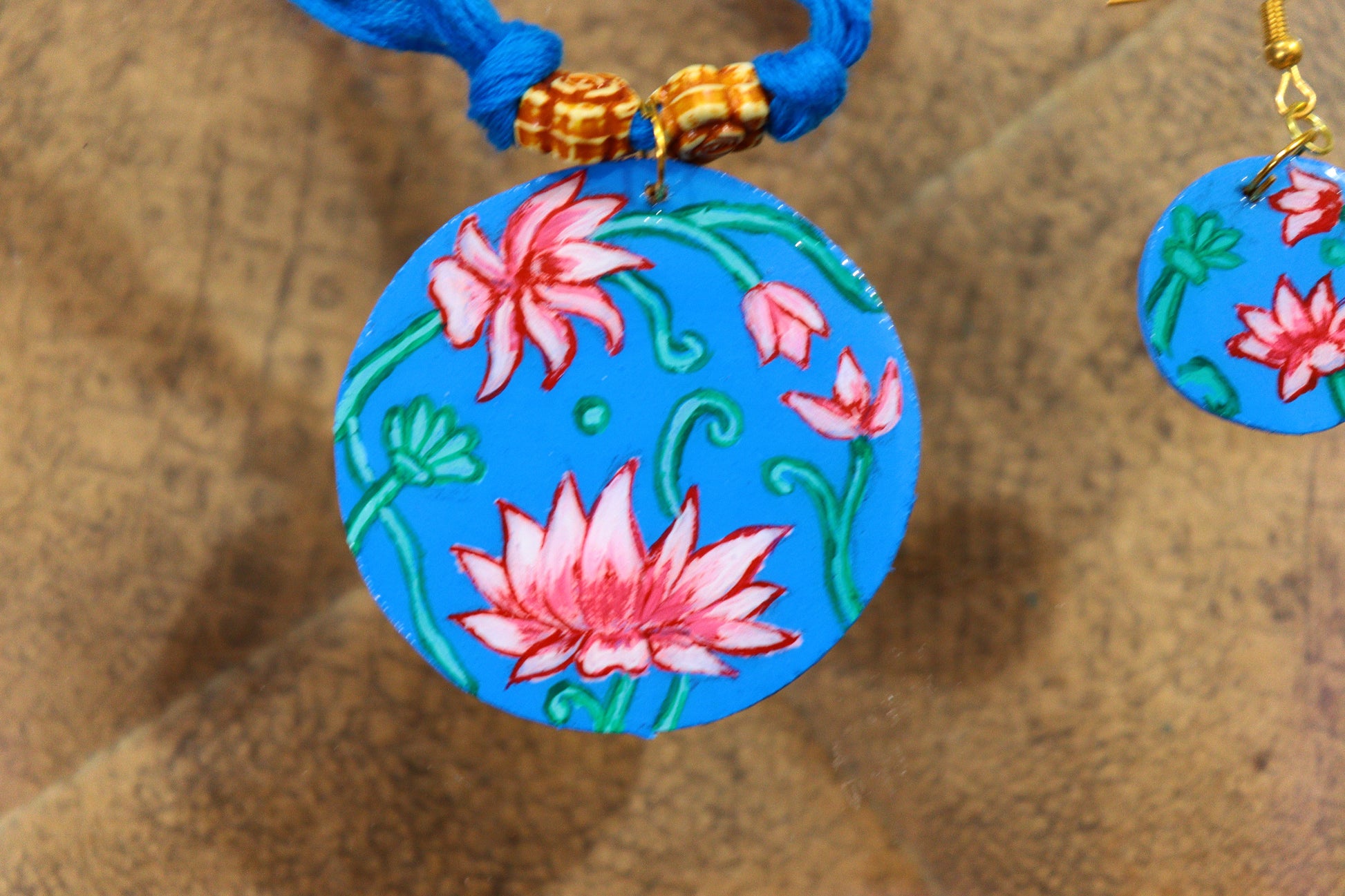 Colorful pendant with floral design on a blue cord against a wooden background