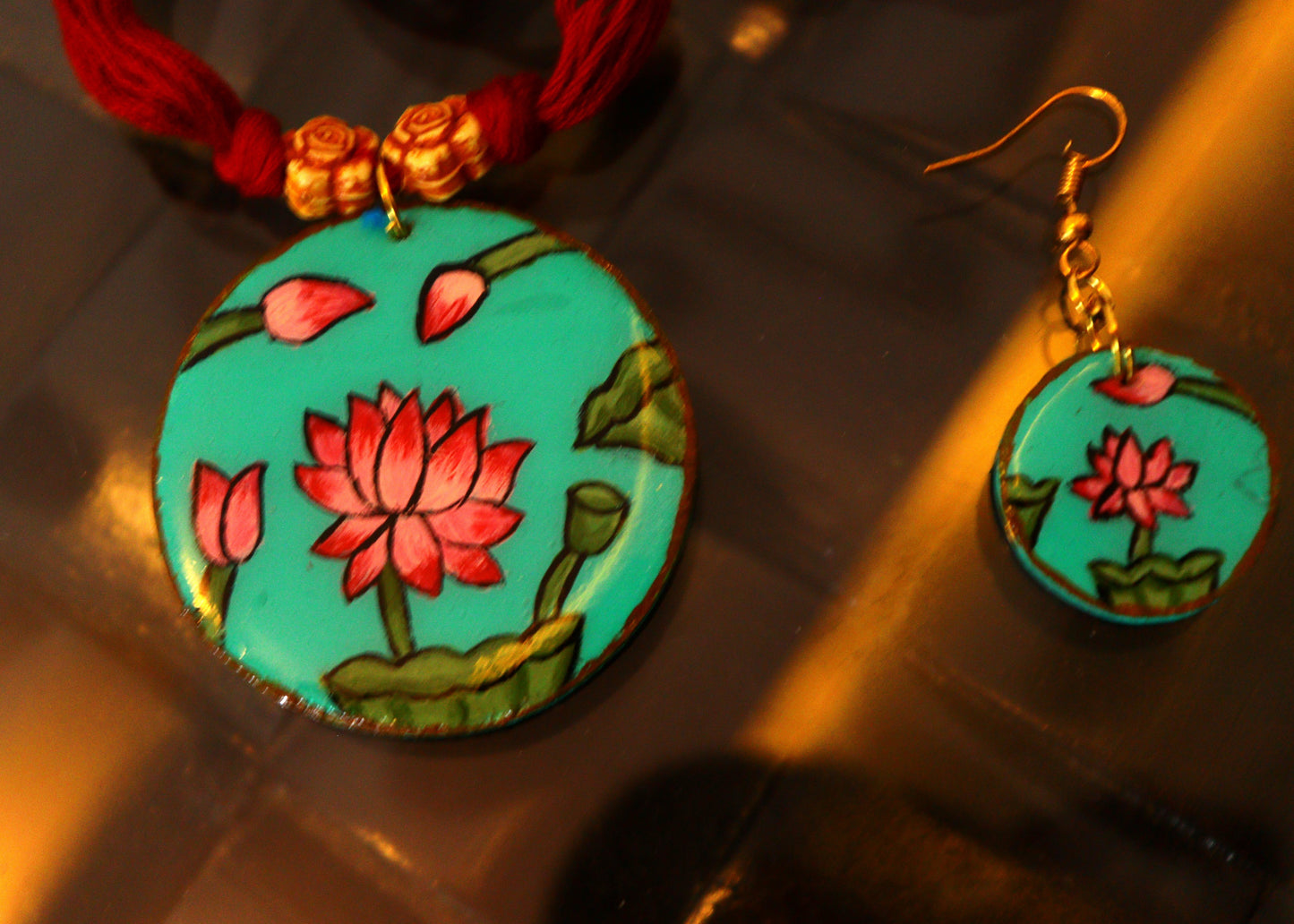 Colorful lotus flower pendant and earrings on a reflective surface