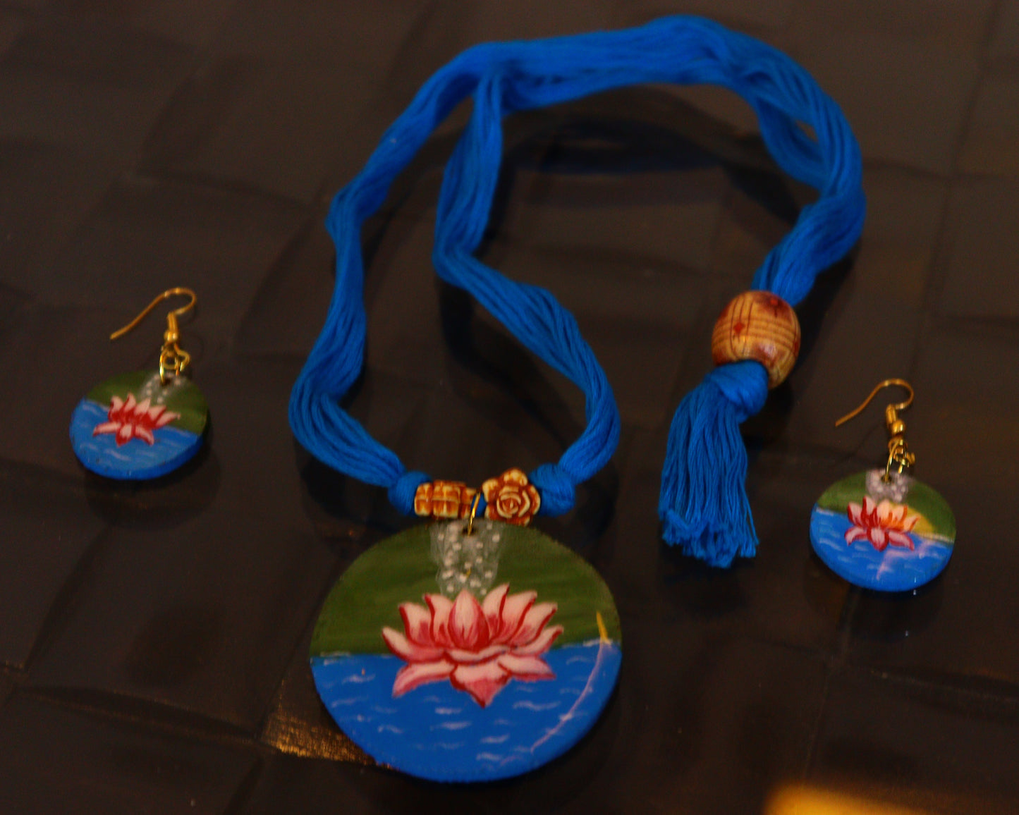 Jewelry set with a necklace and earrings featuring lotus designs on a dark surface.