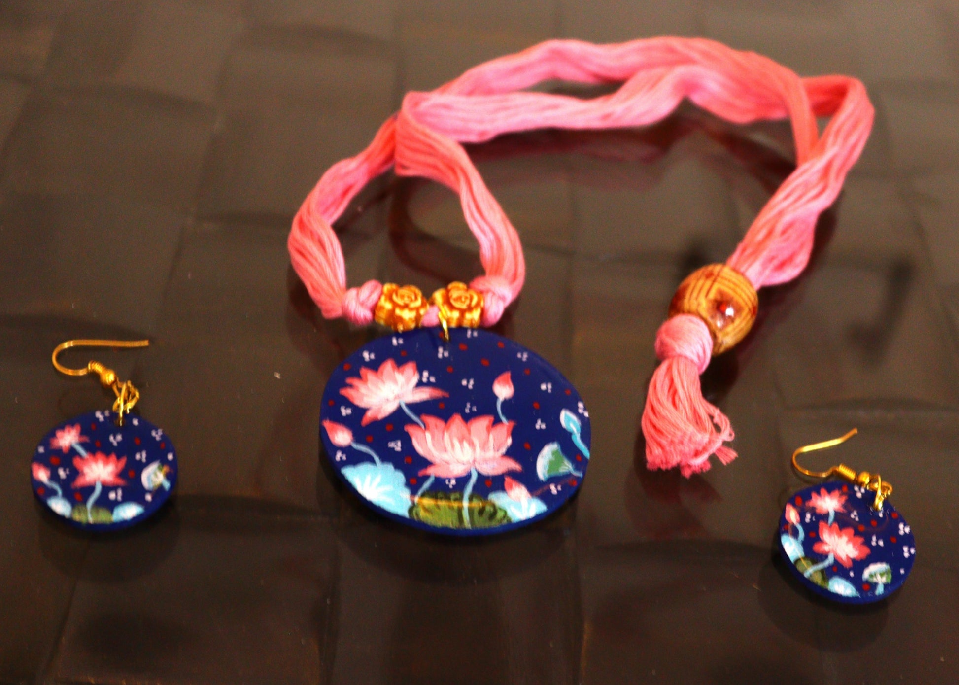 Colorful necklace with floral pendant and matching earrings on a reflective surface