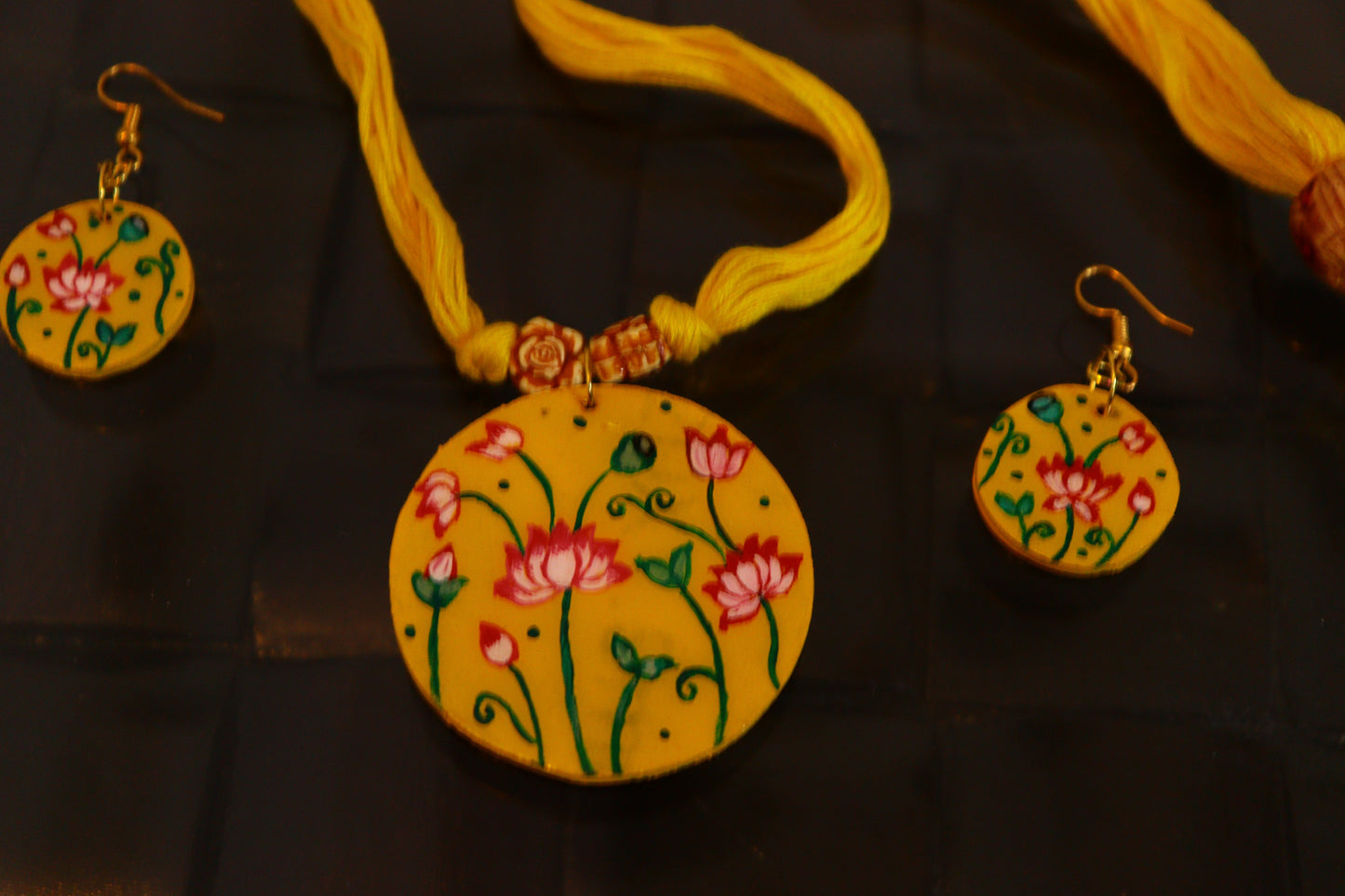 Yellow necklace with floral design and matching earrings on a dark background