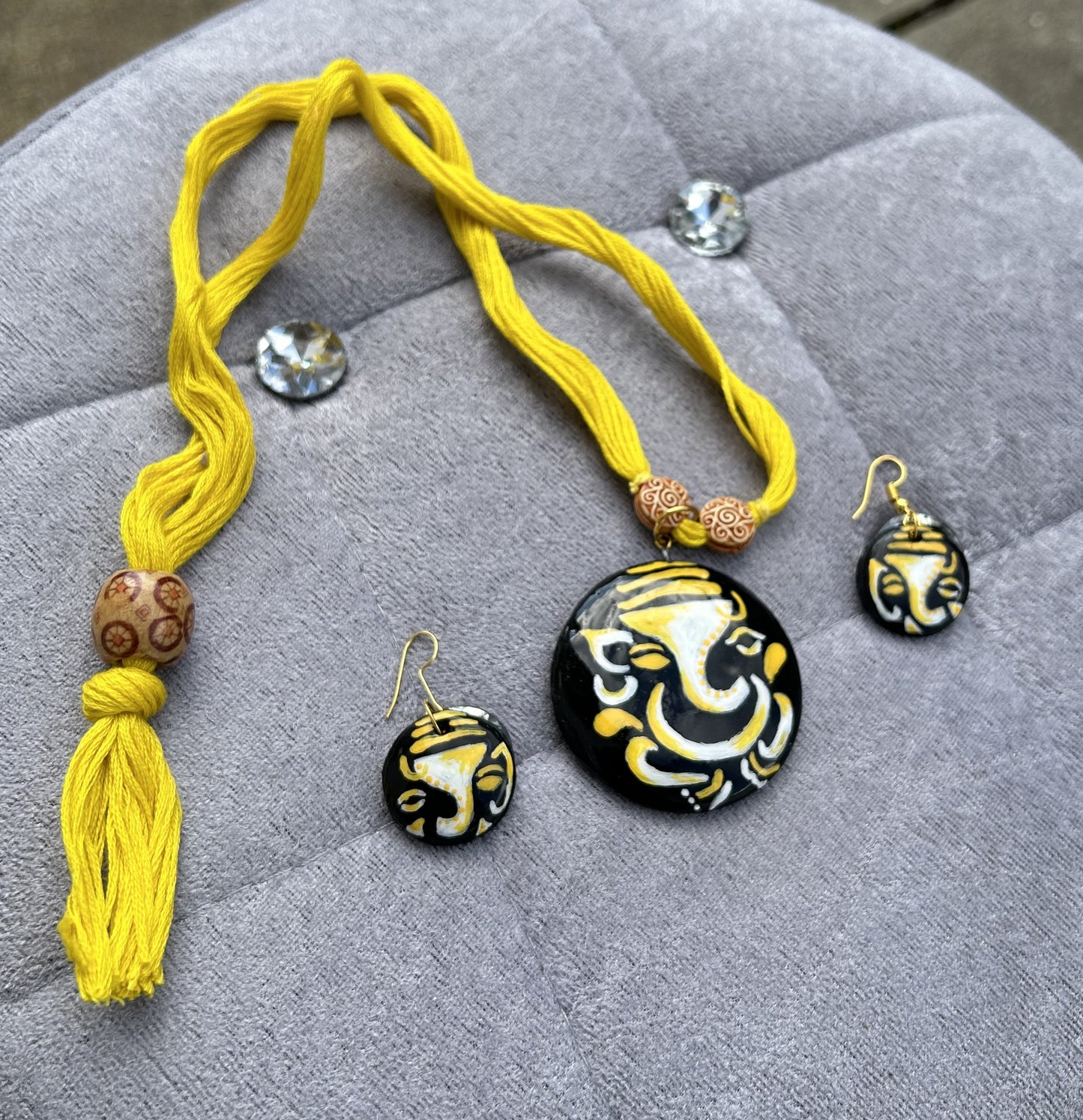 Yellow necklace and matching earrings with a black and gold design on a gray surface