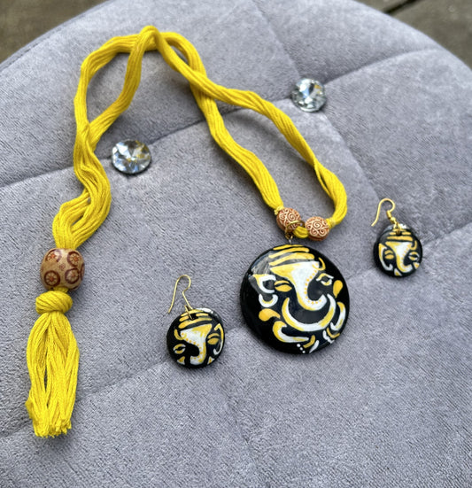 Yellow necklace and matching earrings with a black and gold design on a gray surface