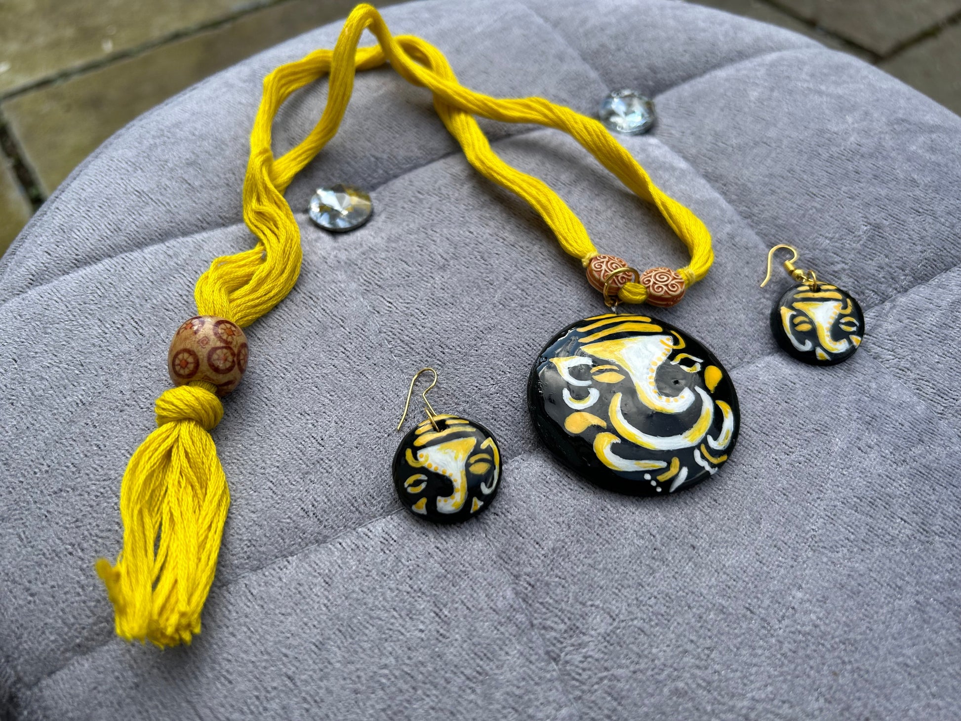 Necklace and earrings with yellow tassels and black and gold designs on a gray surface.