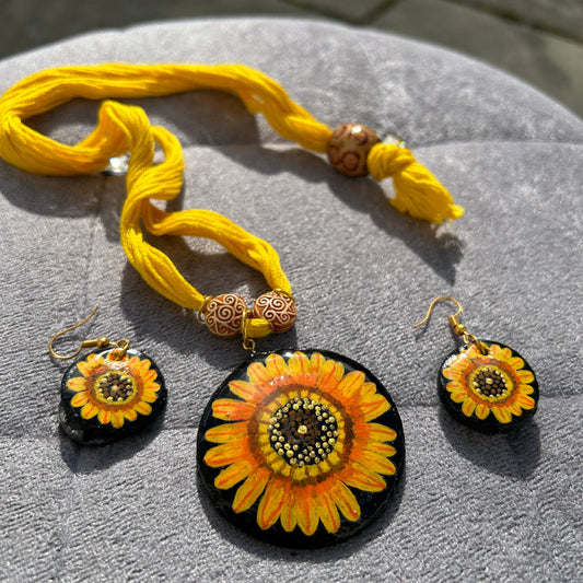 Sunflower-themed jewelry set including a necklace and earrings on a textured surface.