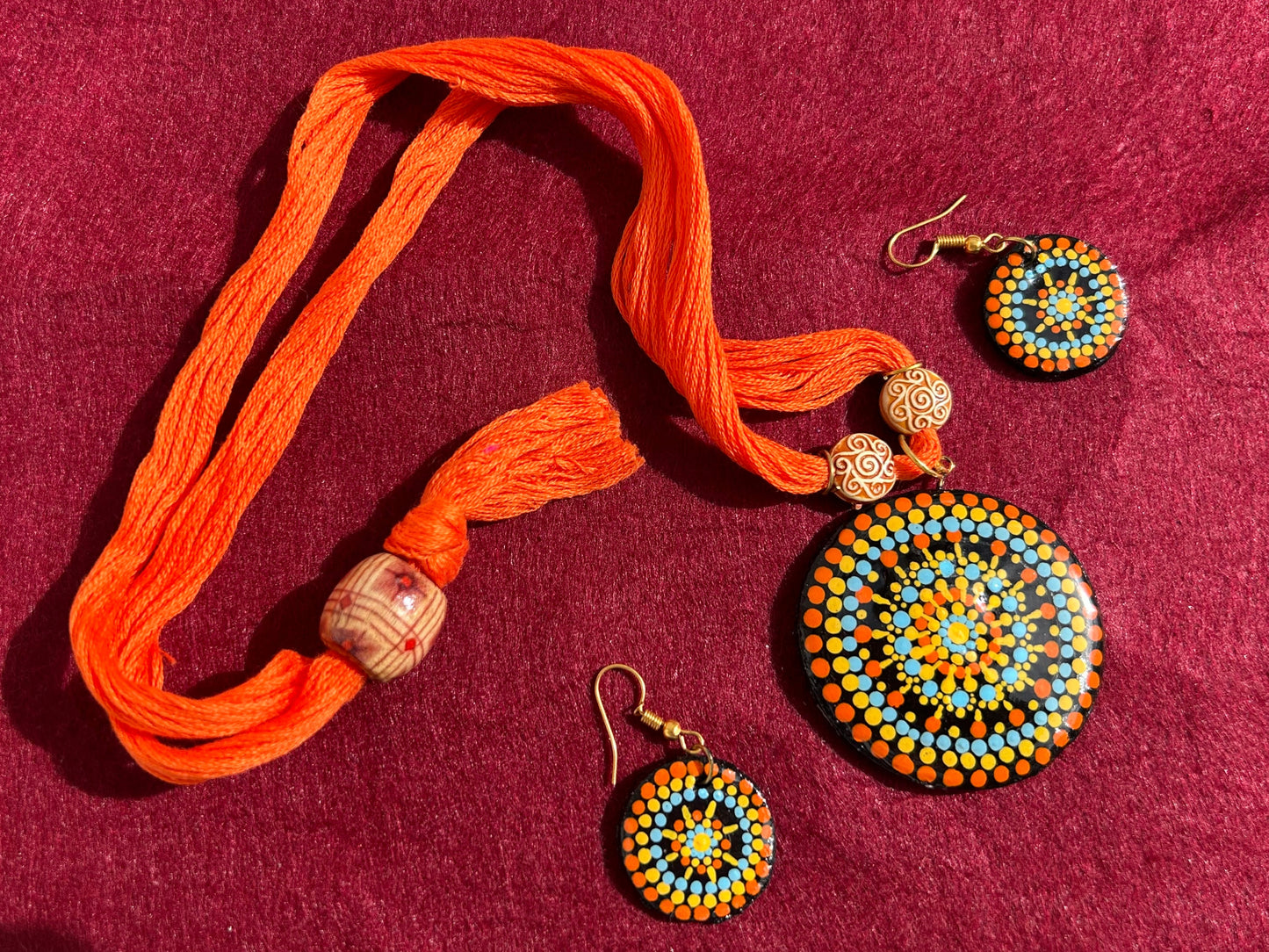 Colorful beaded earrings with an orange cord on a maroon fabric background