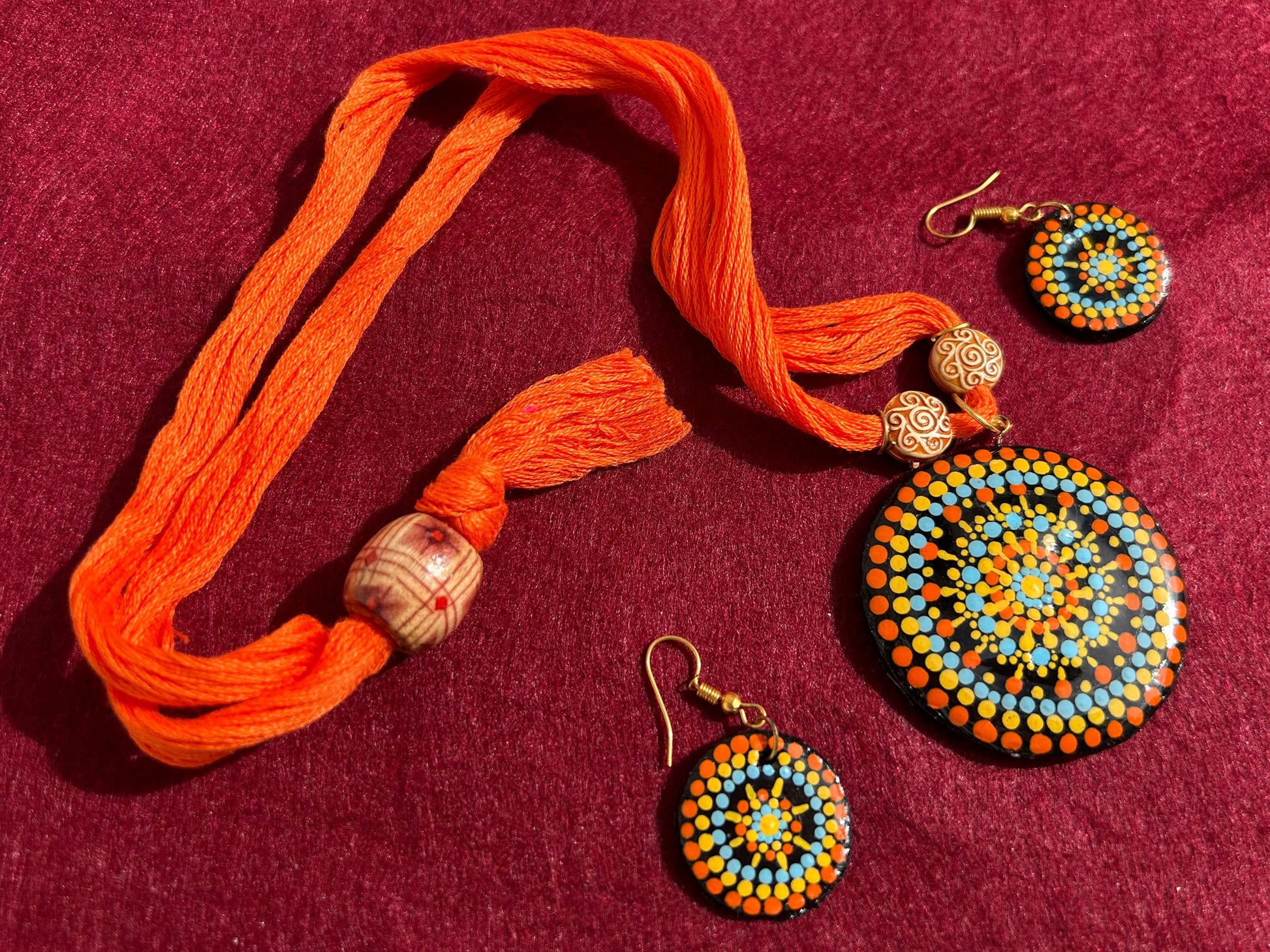 Jewelry set with orange necklace and beaded earrings on a maroon background