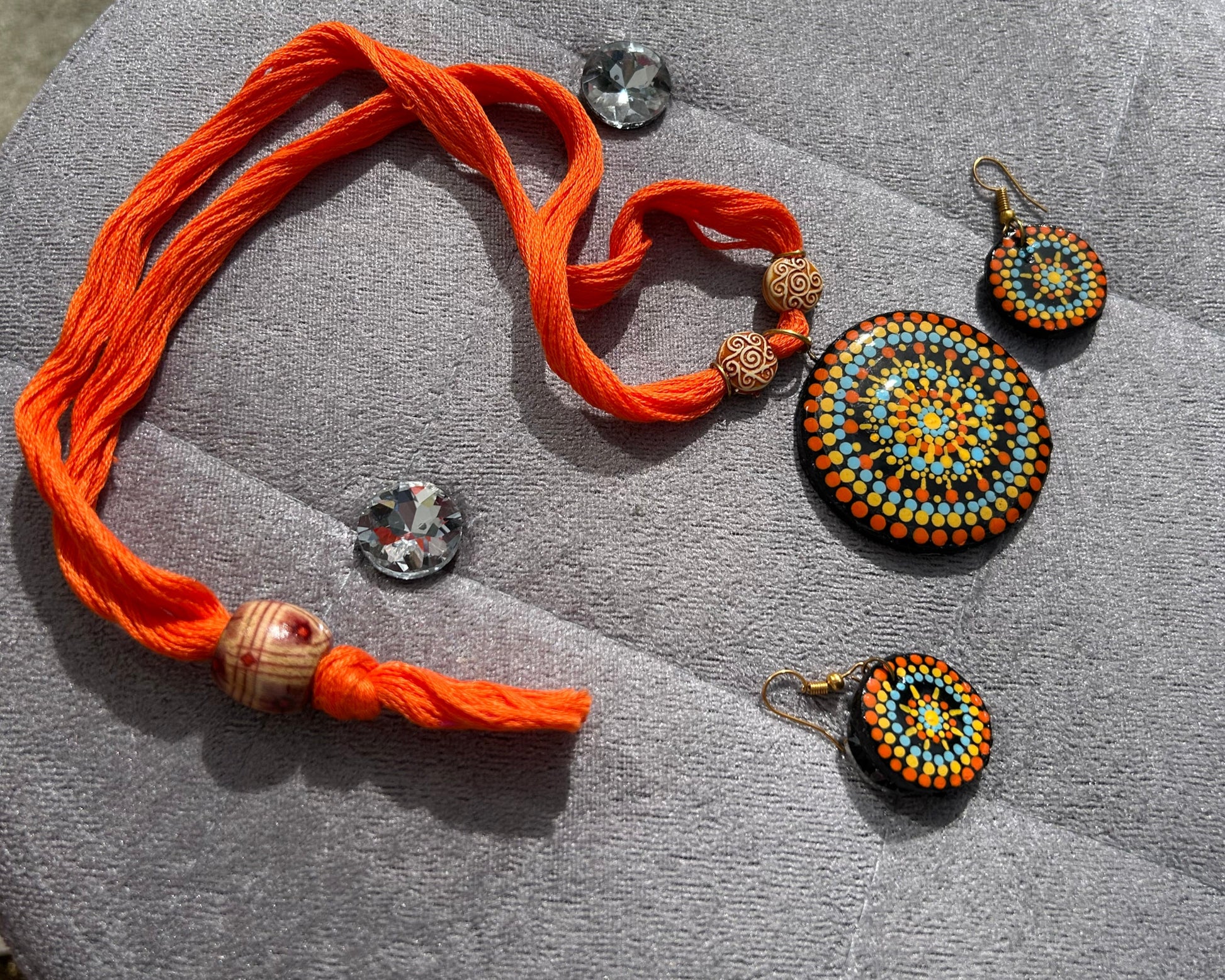 Jewelry set with orange thread bracelet and beaded earrings on a gray surface