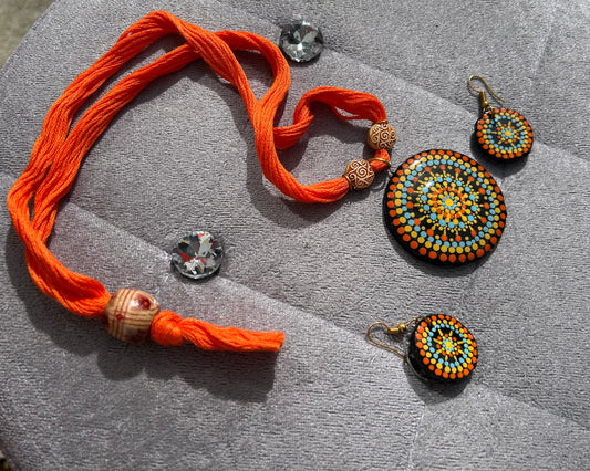 Jewelry set with orange thread bracelet and beaded earrings on a gray surface