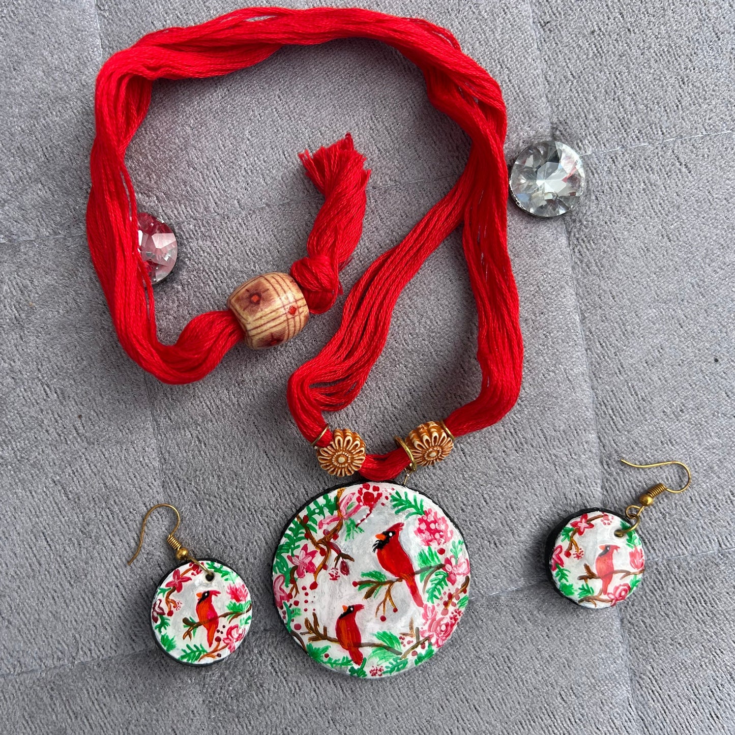 Set of earrings with floral and bird design on a red thread against a gray background