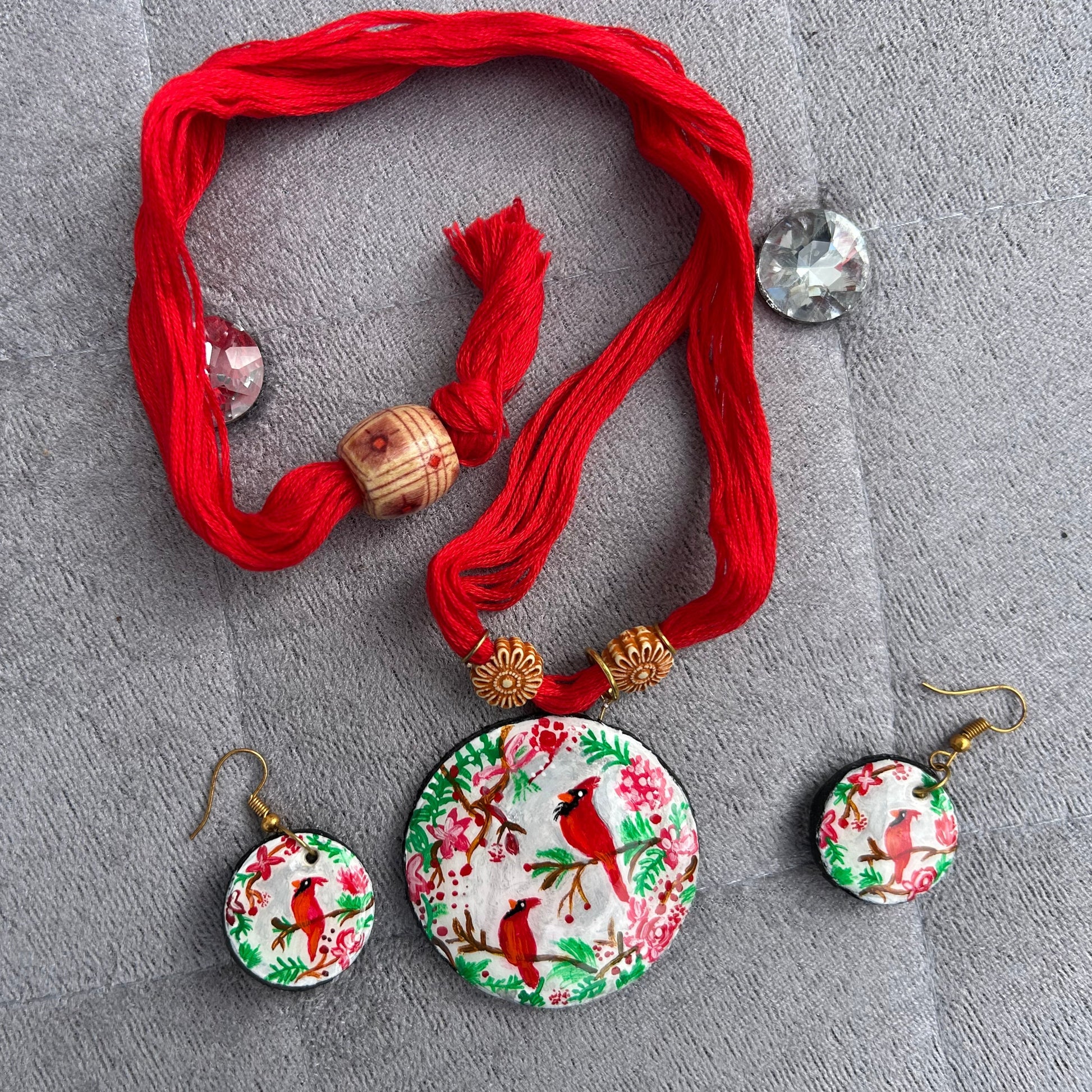 Set of earrings with floral and bird design on a red thread against a gray background