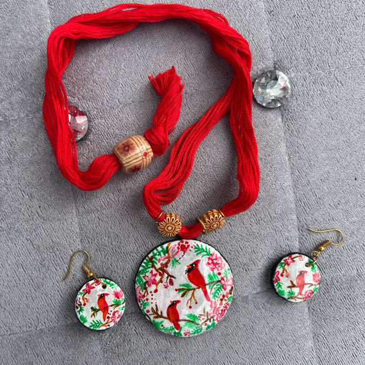 Set of earrings with floral and bird design on a red thread against a gray background