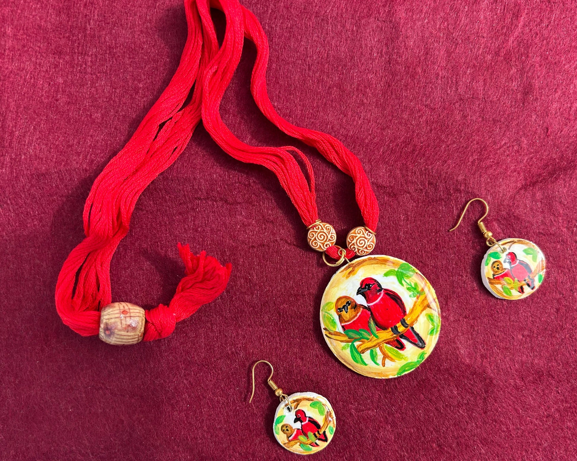 Jewelry set with red tassels and bird-themed pendants on a maroon fabric background
