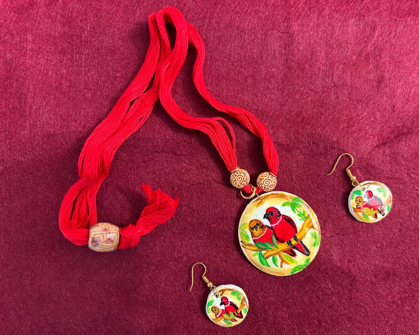 Jewelry set with red tassels and bird-themed pendants on a red fabric background