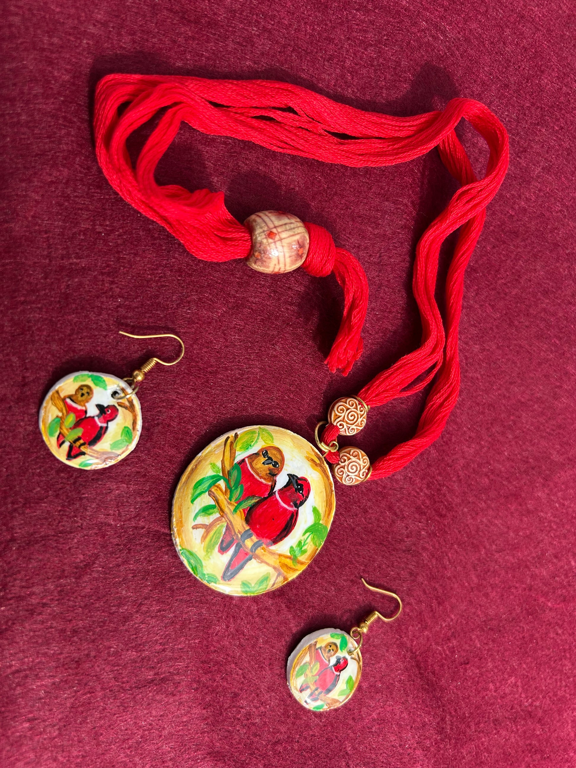 Jewelry set with red tassels and bird-themed pendants on a maroon background