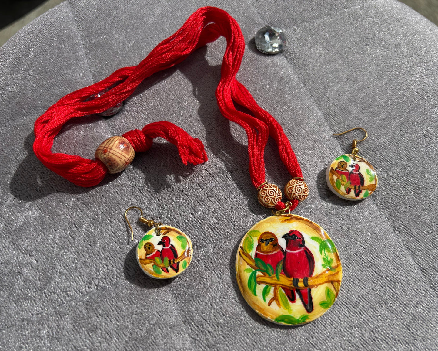 Jewelry set with red tassels and bird-themed pendants on a gray surface