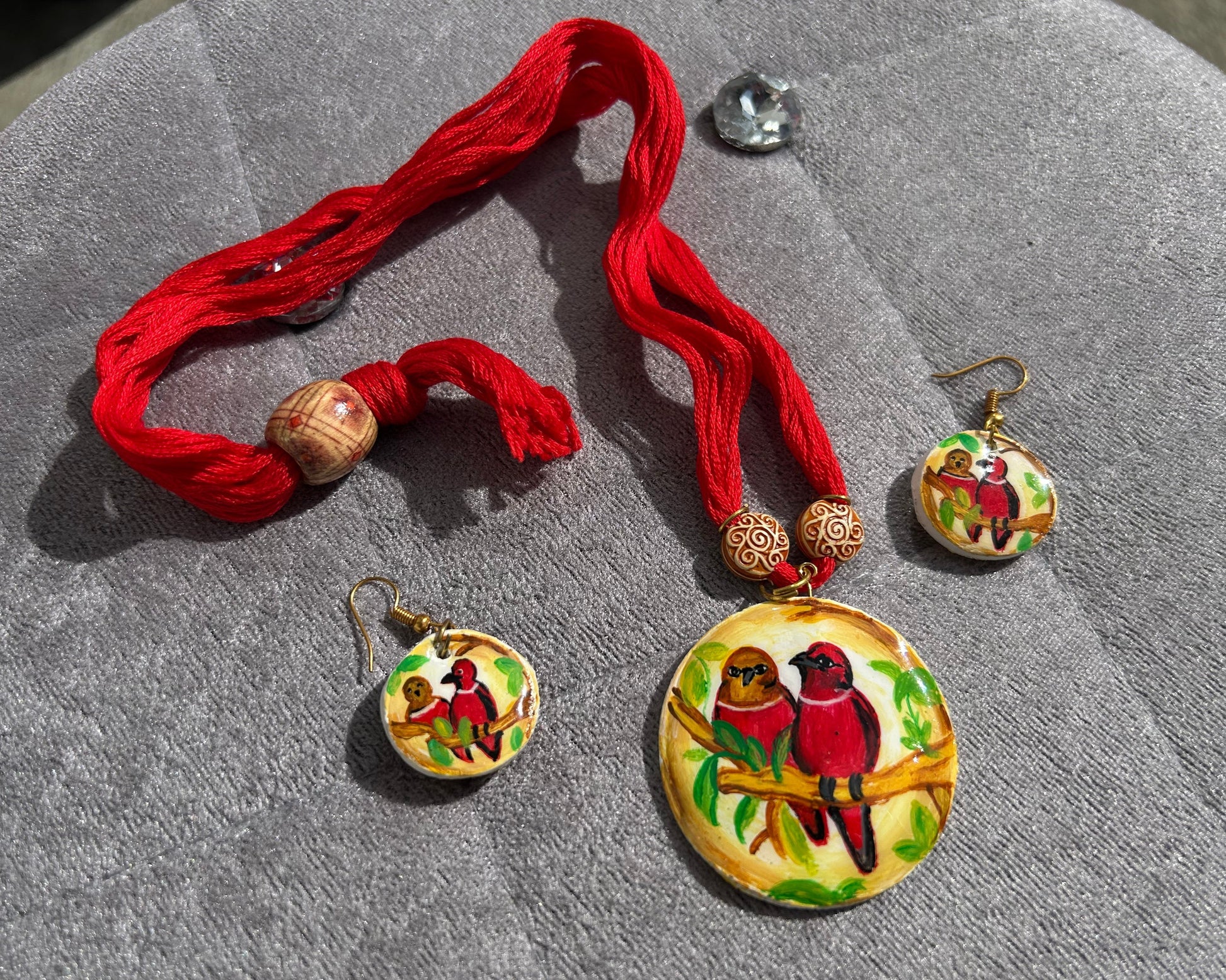 Jewelry set with red tassels and bird-themed pendants on a gray surface