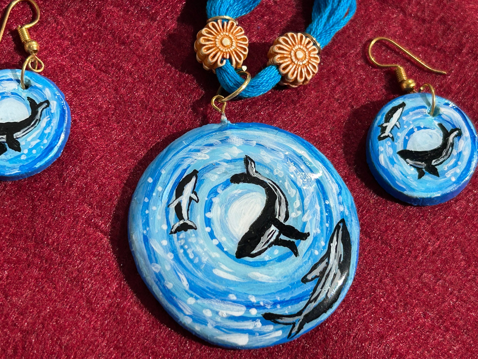 Jewelry set with blue circular pendants and whale designs on a red background