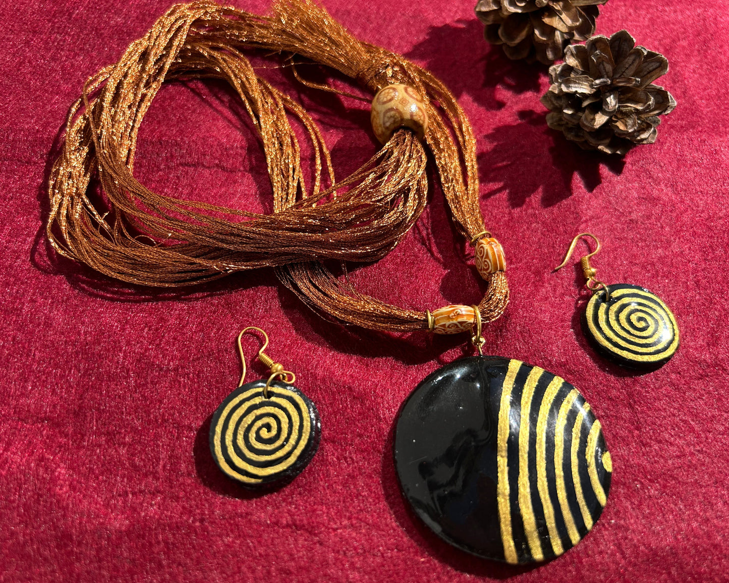 Jewelry set with spiral-patterned pendant and earrings on a red fabric background