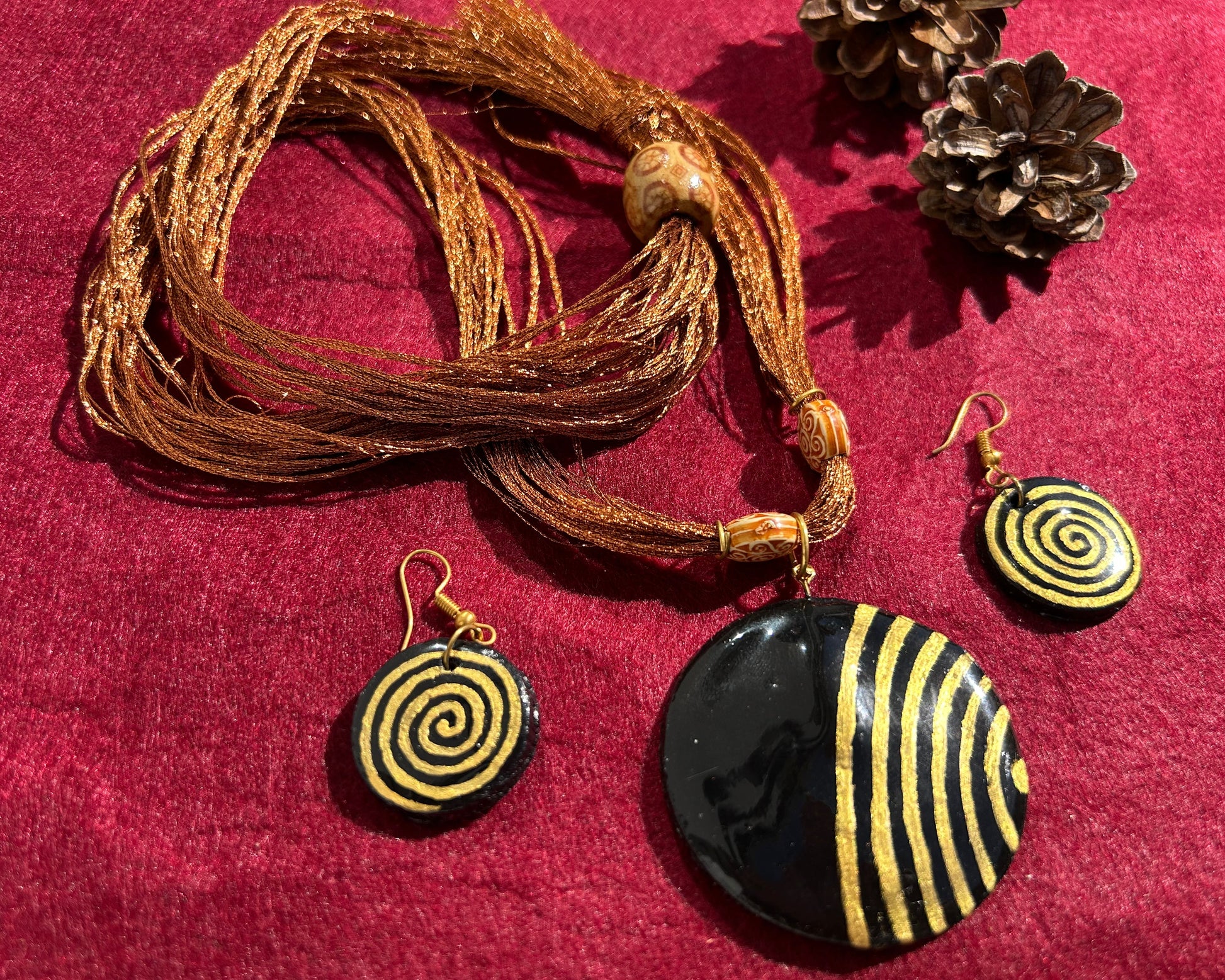 Jewelry set with spiral-patterned pendant and earrings on a red fabric background