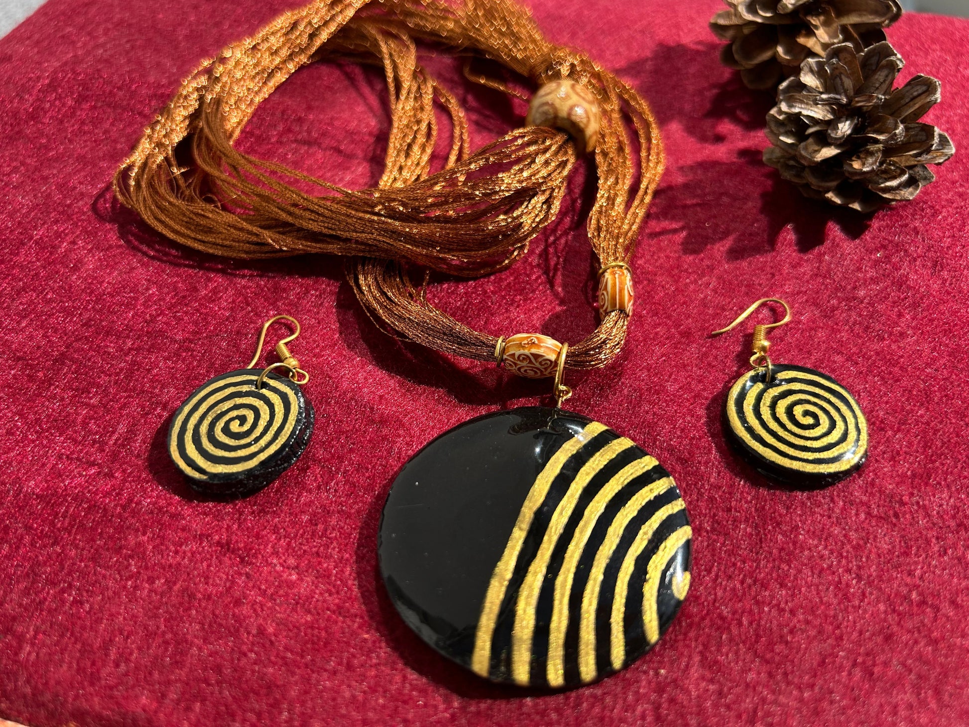 Black and gold spiral pendant necklace and earrings on a red fabric background
