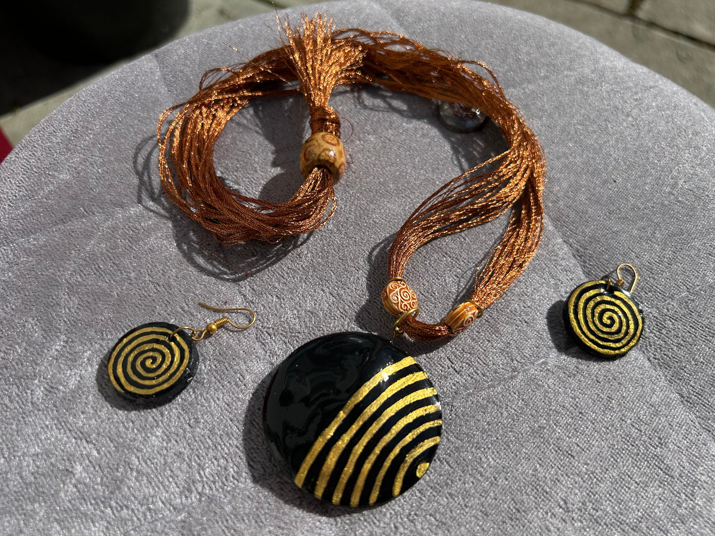Jewelry set with black and gold spiral pendant and matching earrings on a textured surface.