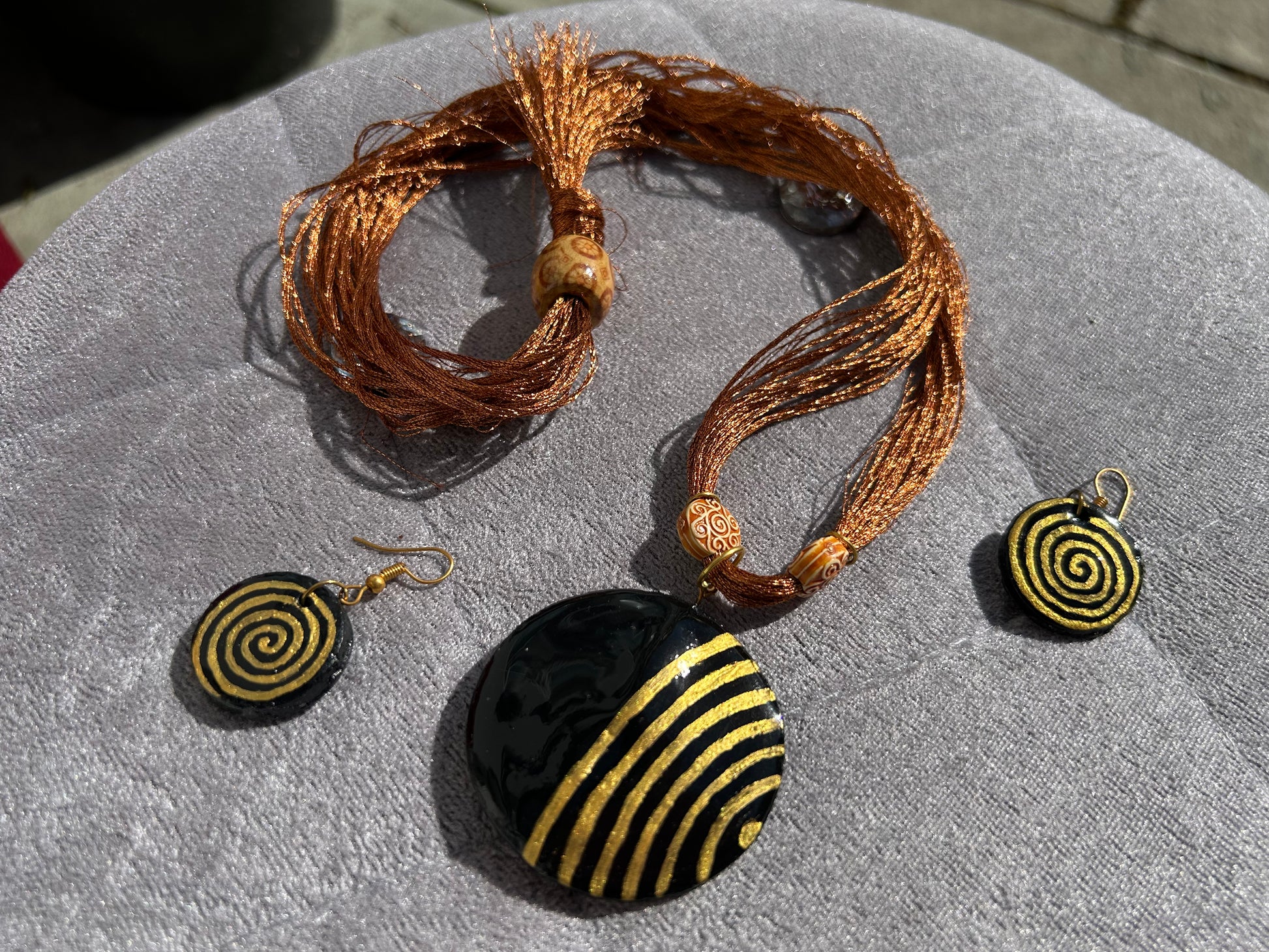 Jewelry set with black and gold spiral pendant and matching earrings on a textured surface.