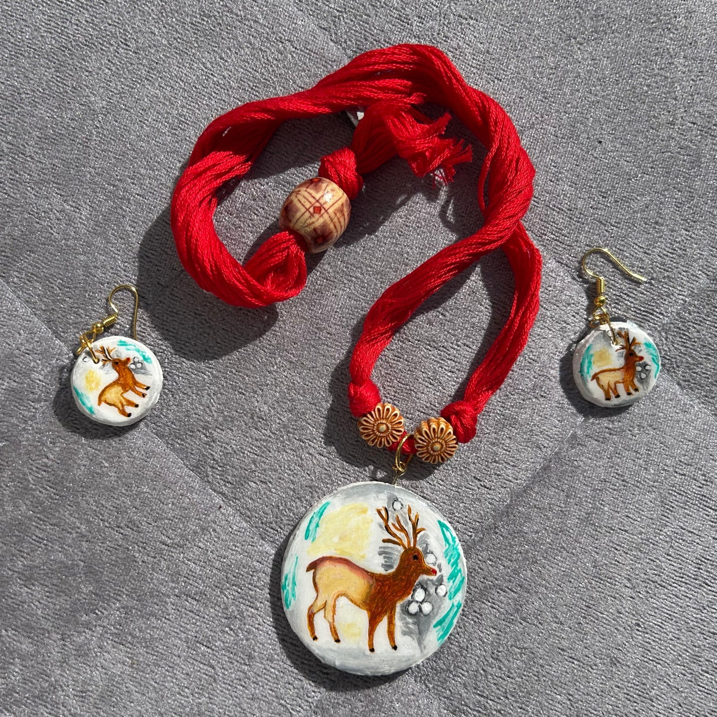 Bracelet with red fabric and deer-themed charms on a gray surface