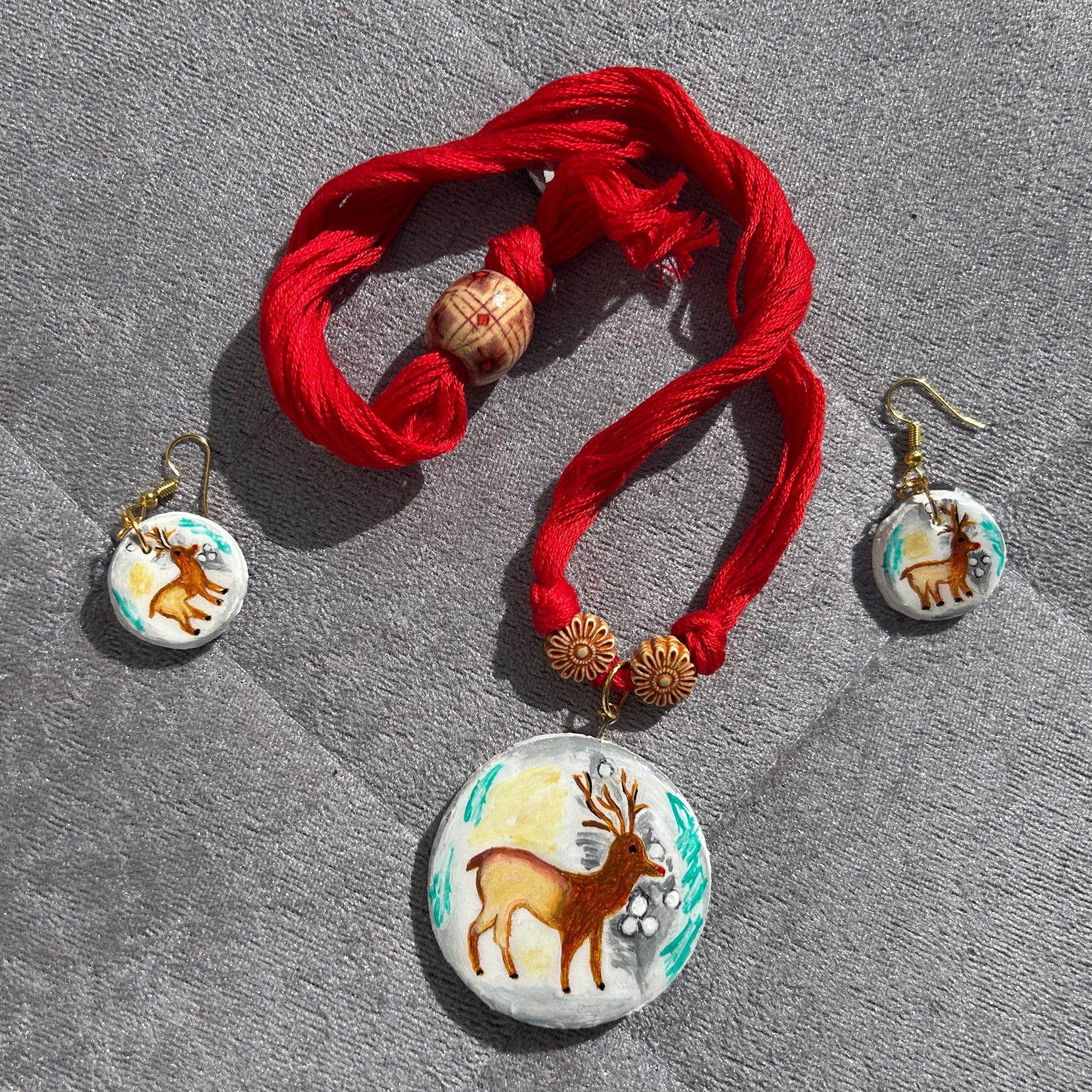 Bracelet with red fabric and deer-themed charms on a gray surface
