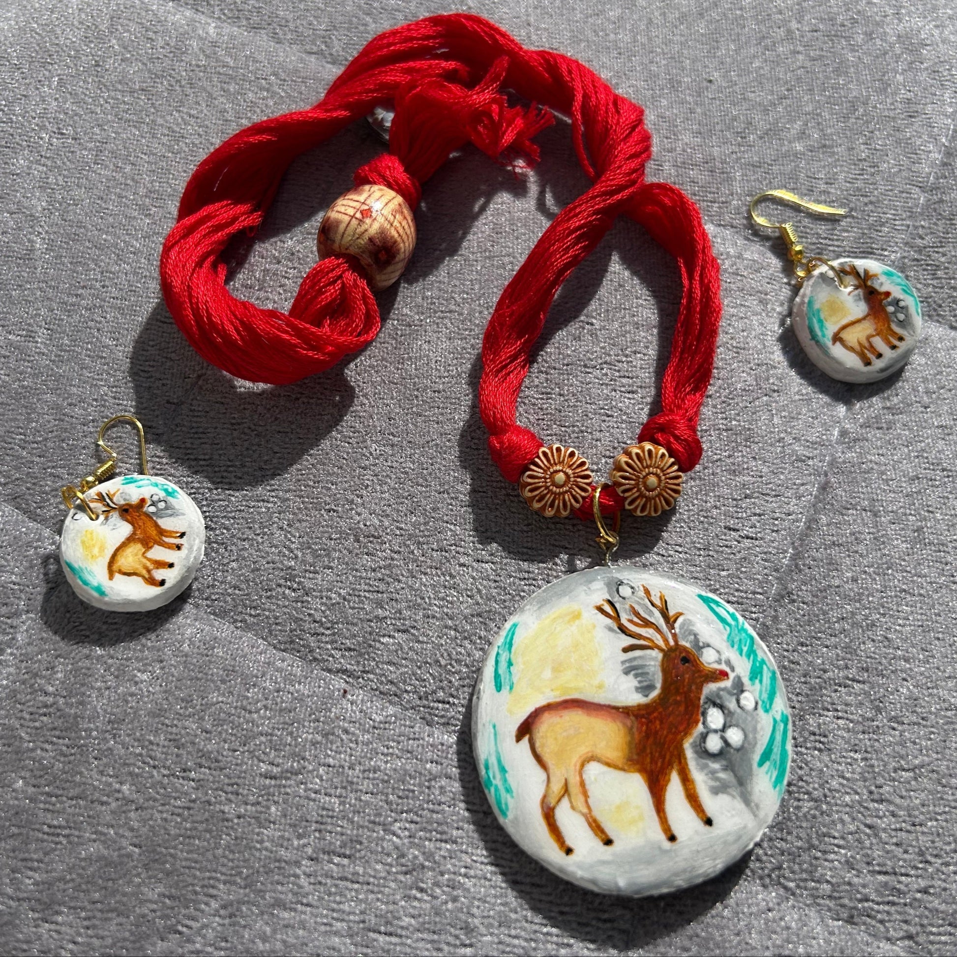 Set of red fabric necklace and matching earrings with deer designs on a gray stone surface