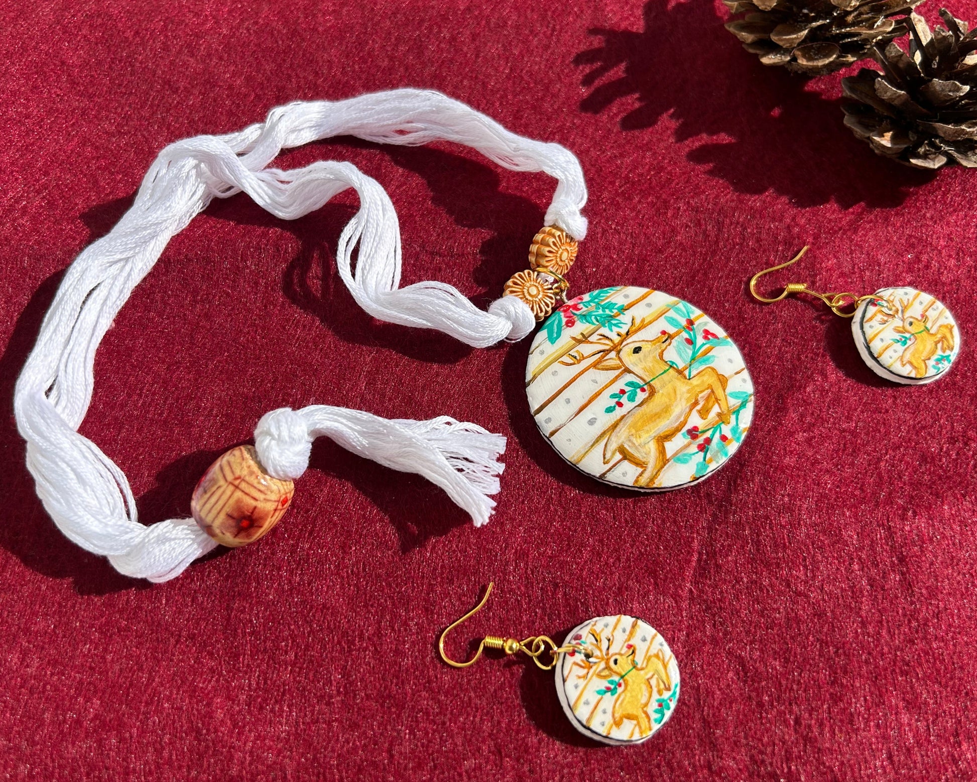 Set of decorative earrings and a necklace with deer design on a red surface