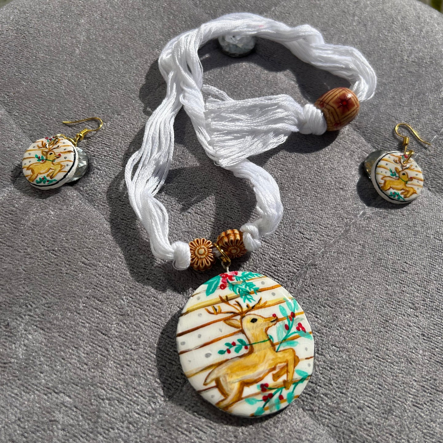 Jewelry set with a necklace and earrings featuring deer designs on a textured surface.
