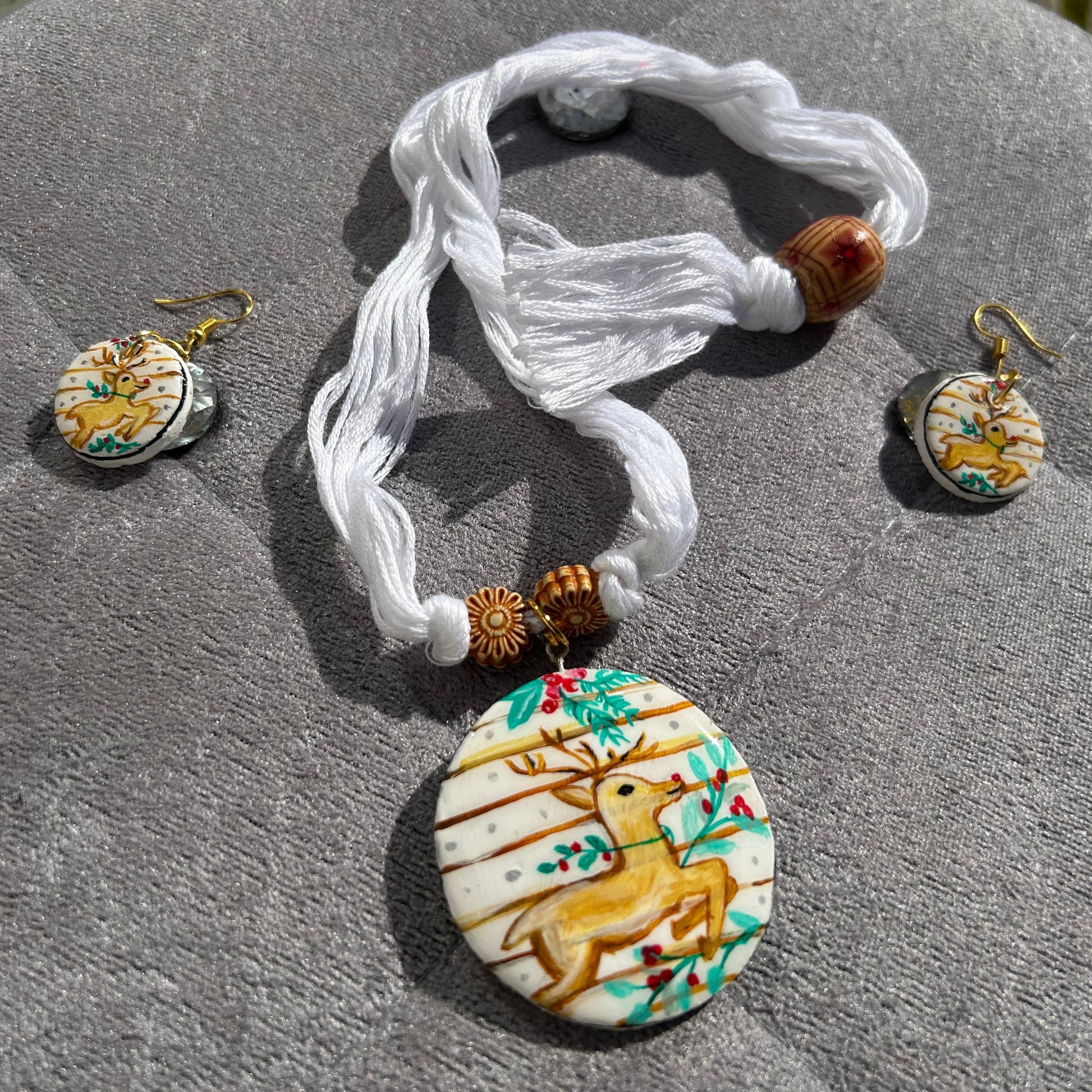 Jewelry set with a necklace and earrings featuring deer designs on a textured surface.