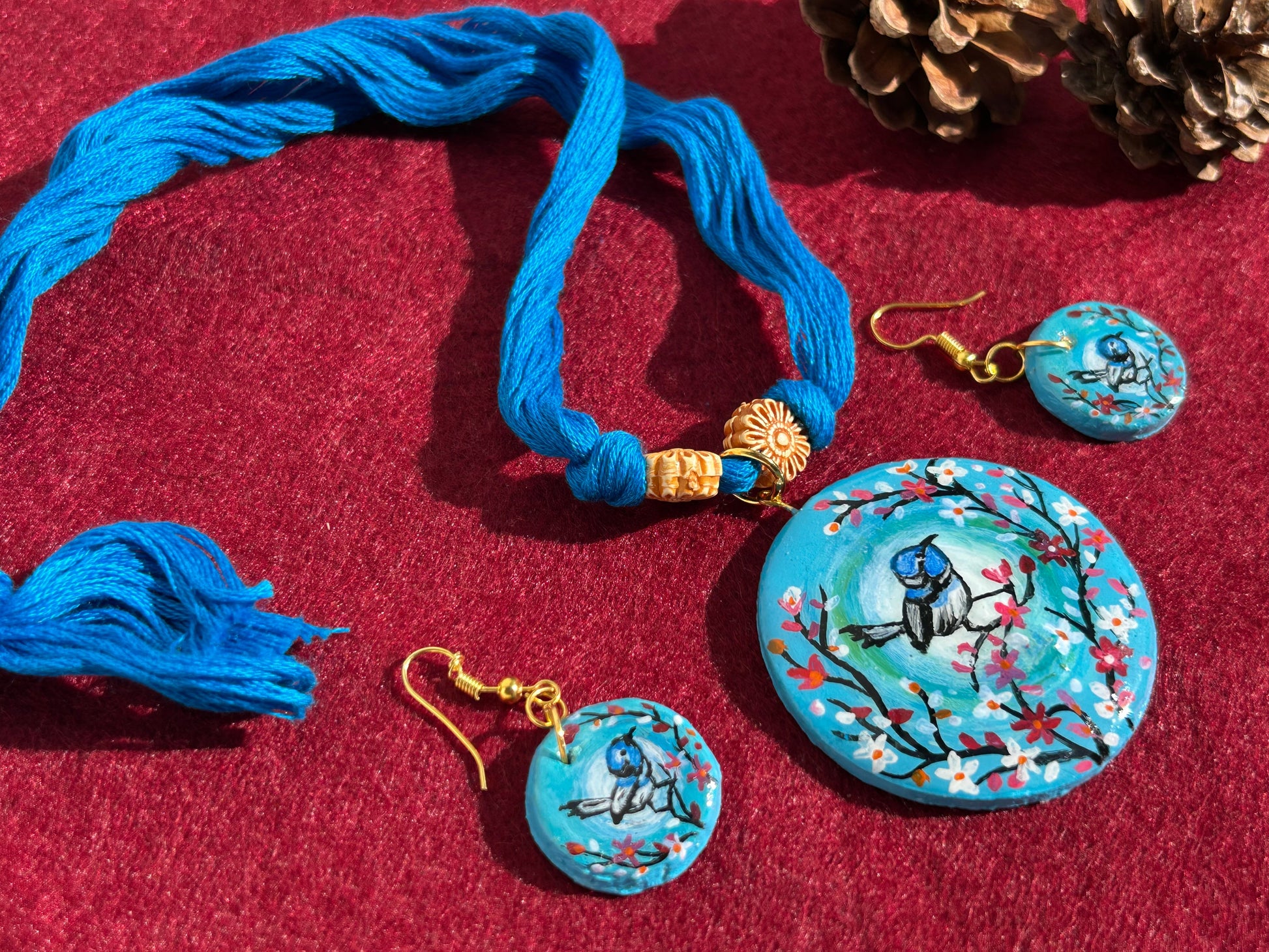 Jewelry set with blue thread, earrings, and a round pendant on a red background