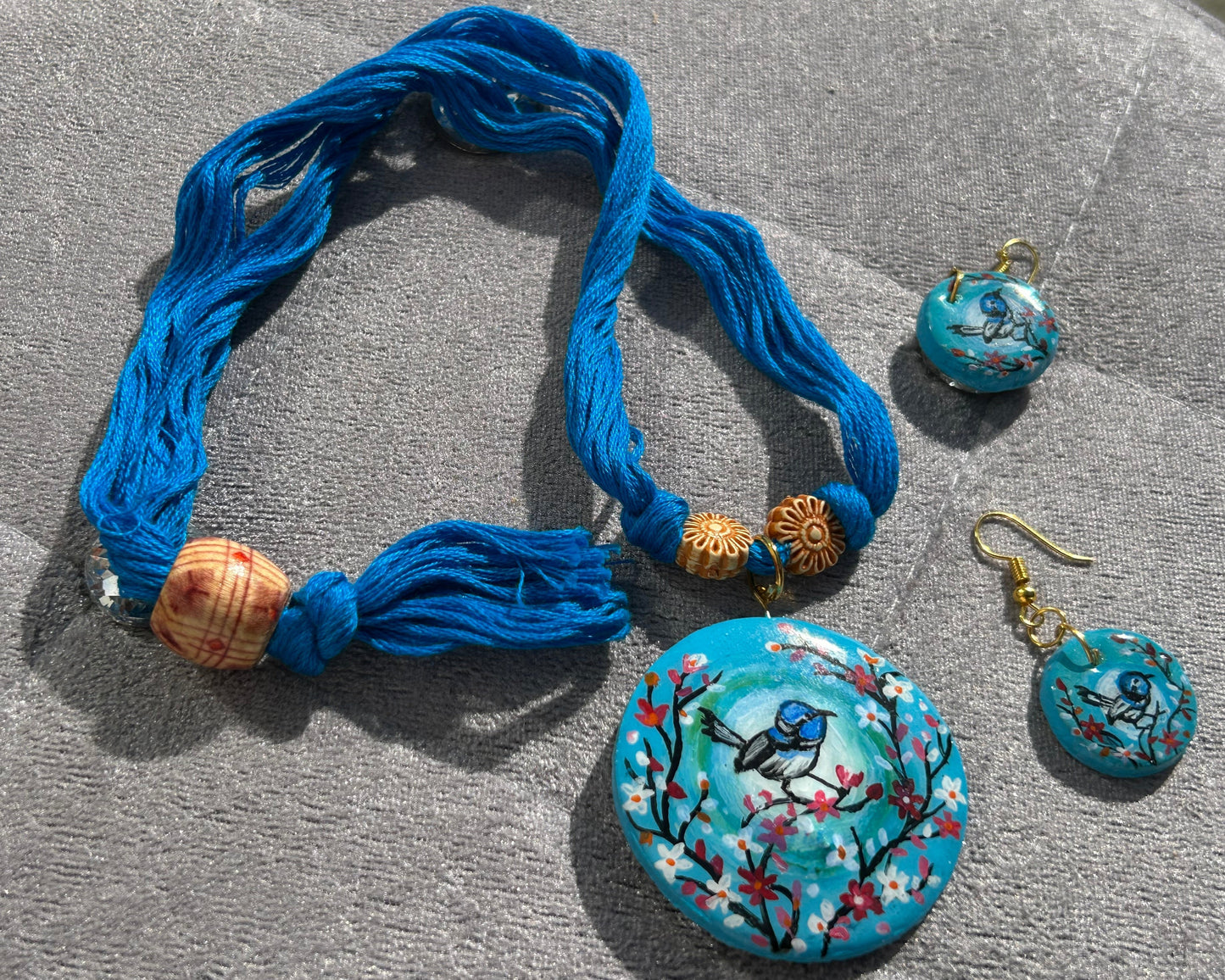 Jewelry set with blue tassel, round pendant, and earrings on a gray surface