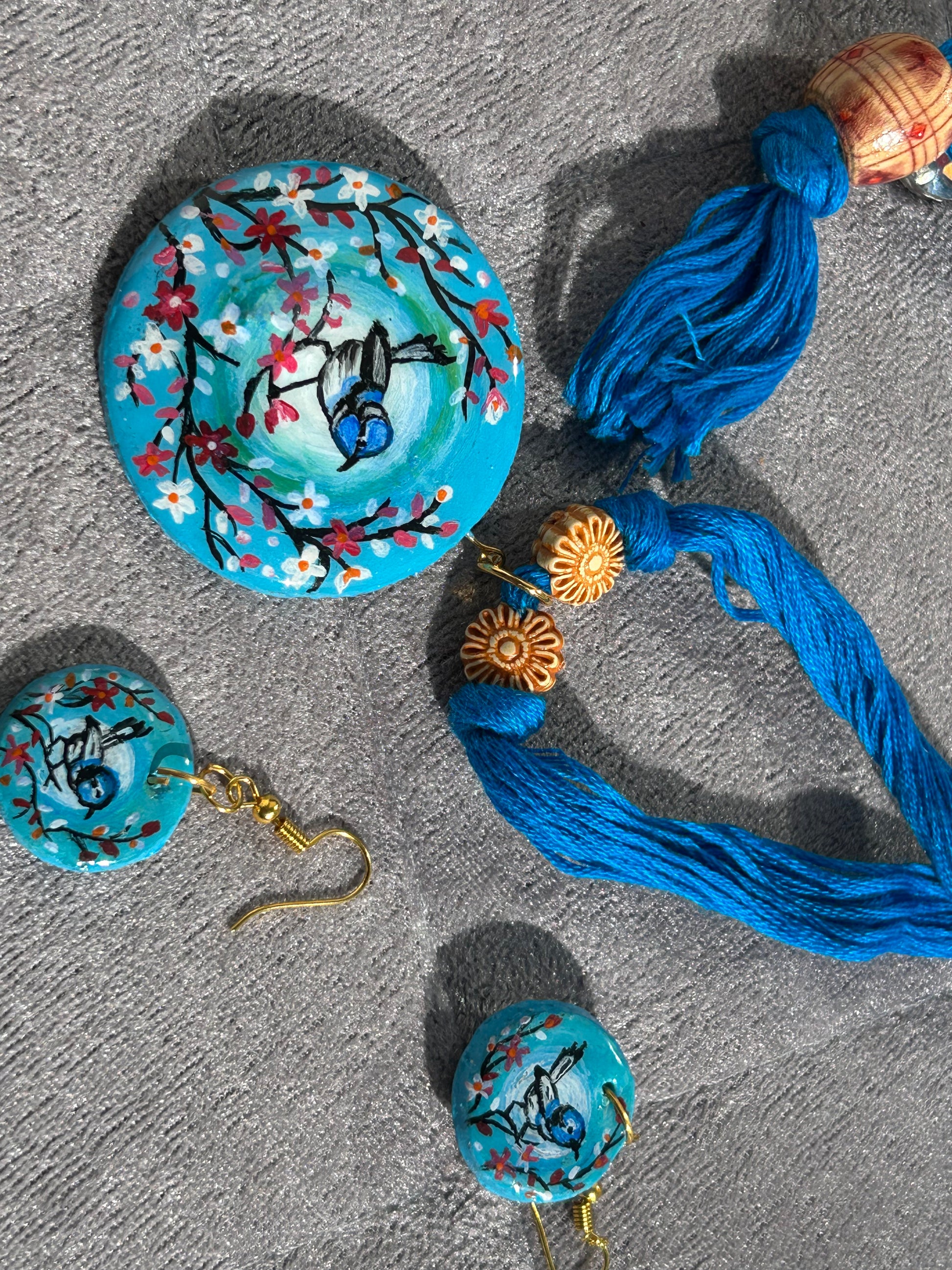 Set of hand-painted earrings with blue thread on a gray surface