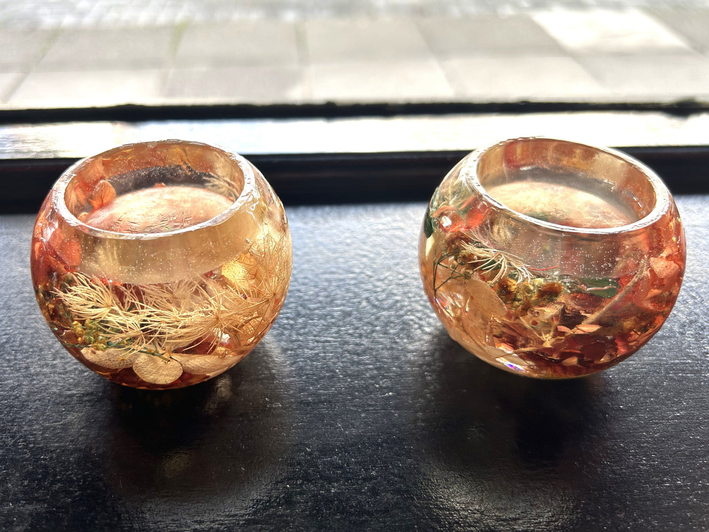 Two decorative Resin candle holder with gold and pink hues on a dark surface.