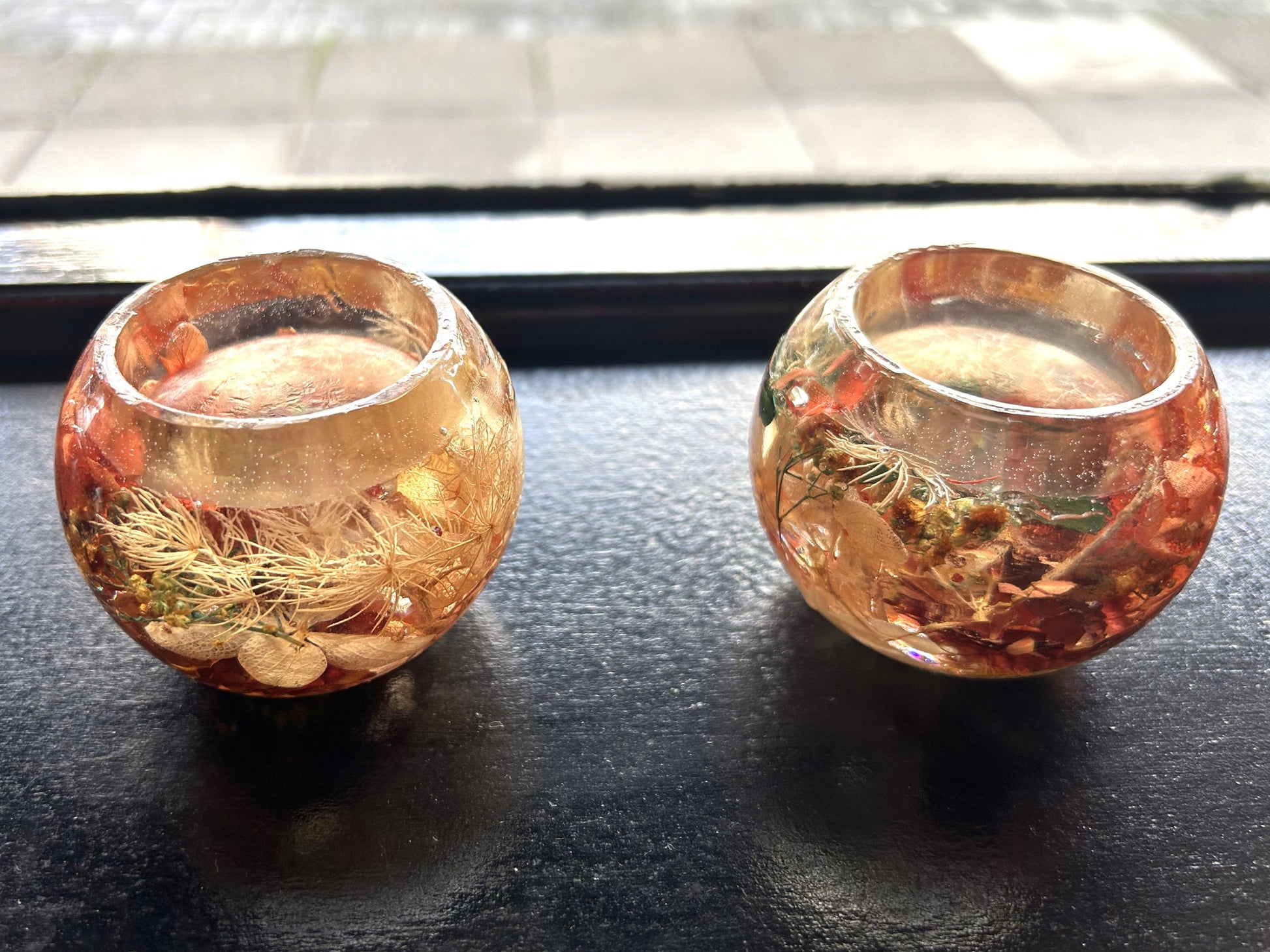 Two decorative Resin candle holder with gold and pink hues on a dark surface.