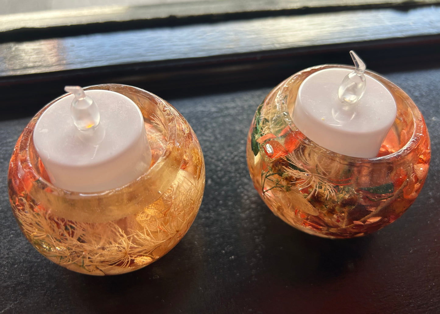 Two decorative candles in glass holders on a dark surface.