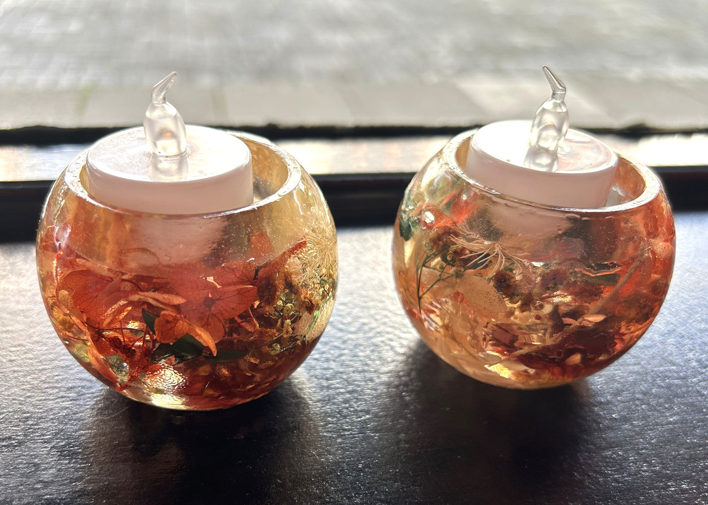 Two small round resin holder with a candle inside on a dark surface.