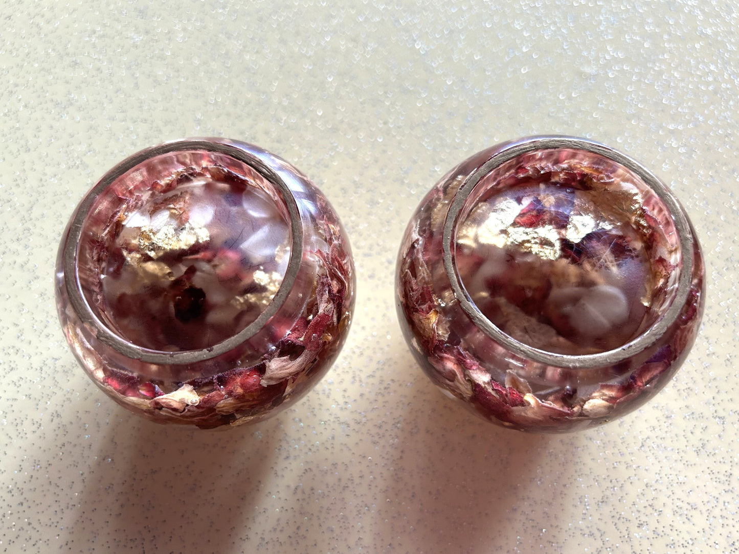 Two small glass jars with pink contents on a light gray surface