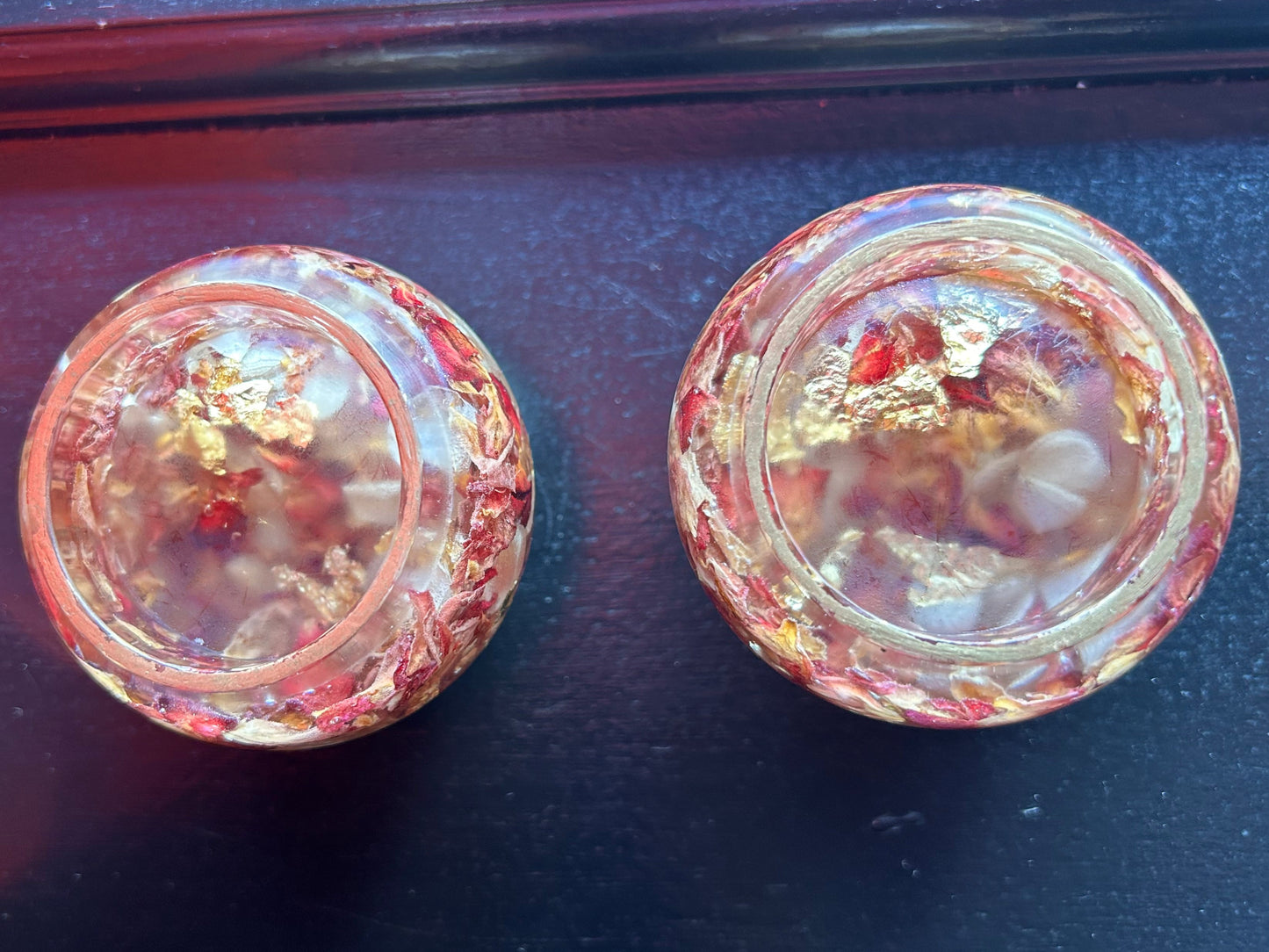 Two round, iridescent glass knobs on a dark surface with red fabric partially visible.