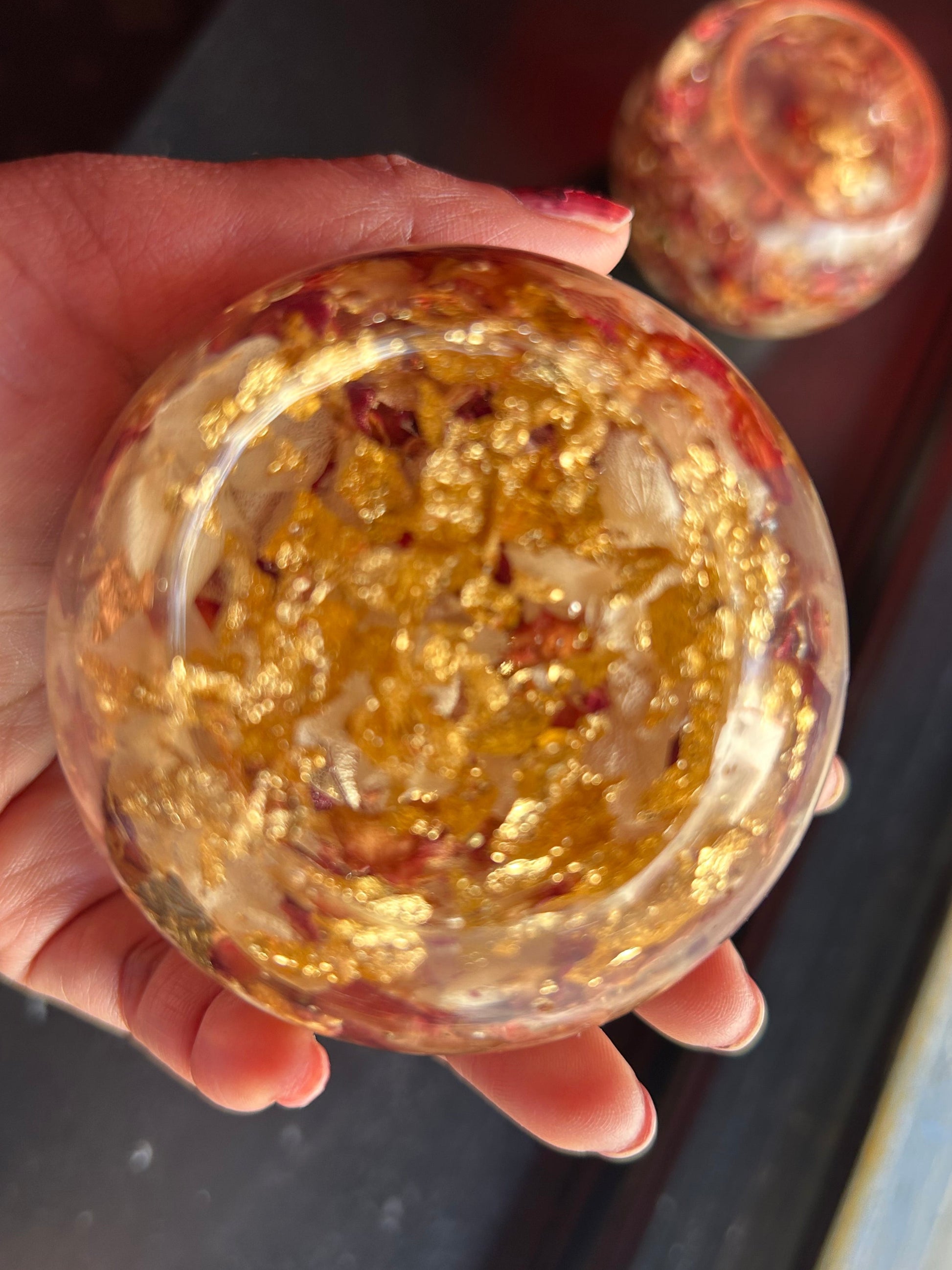 Hand holding a clear crystal ball with gold and red specks against a blurred background