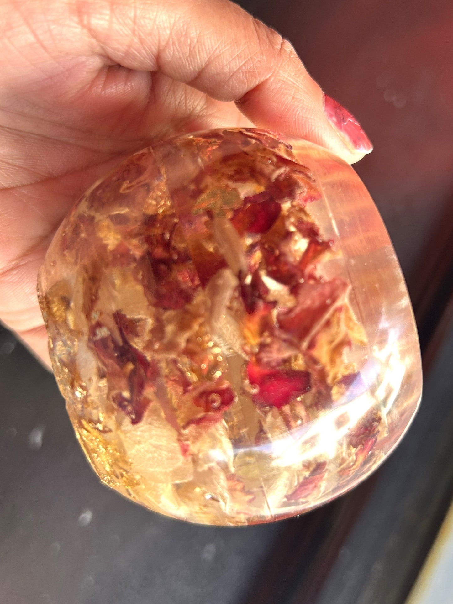 Hand holding a transparent sphere with red and gold contents against a blurred background