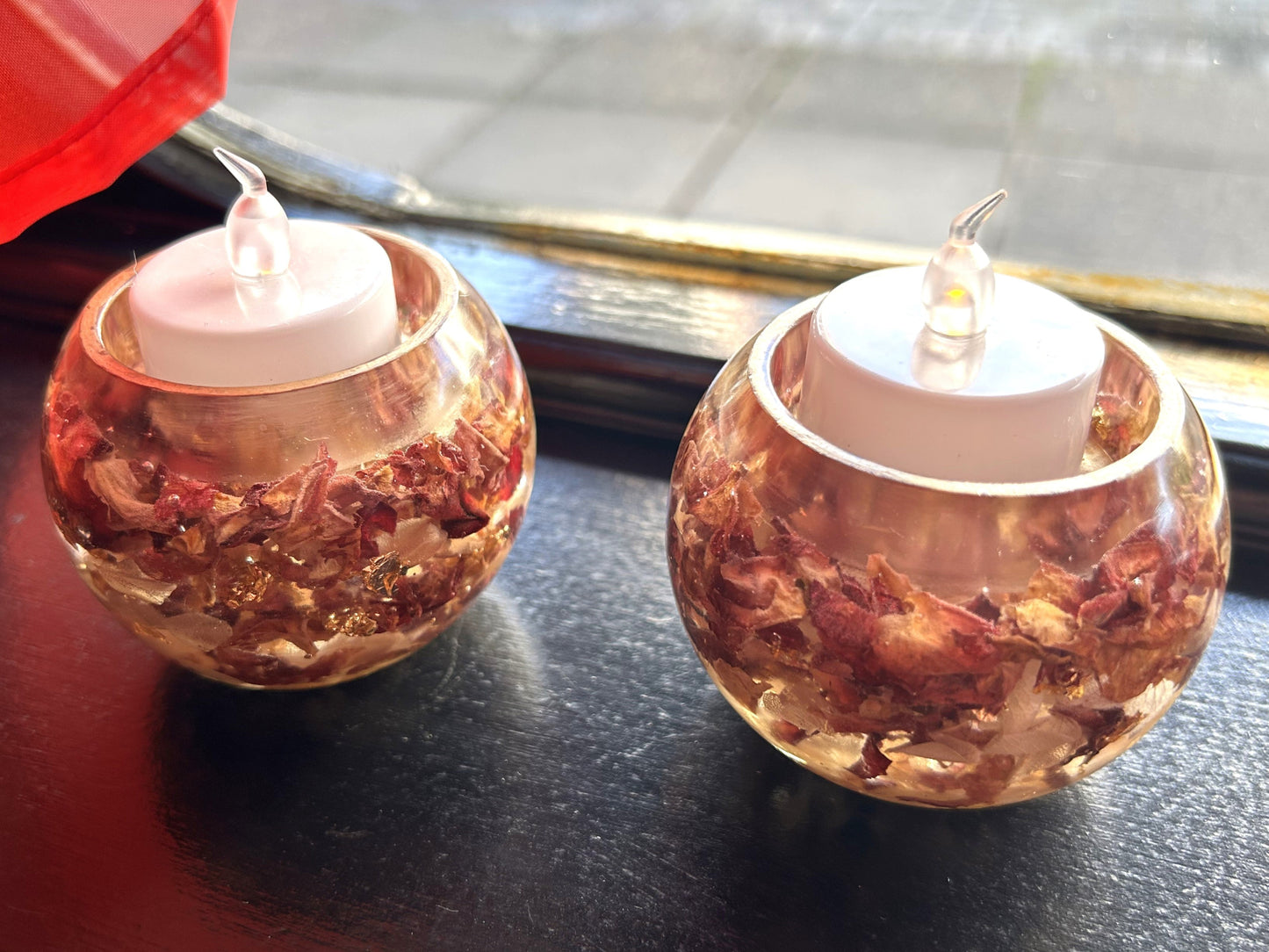 Two small round candles in decorative holders on a reflective surface.
