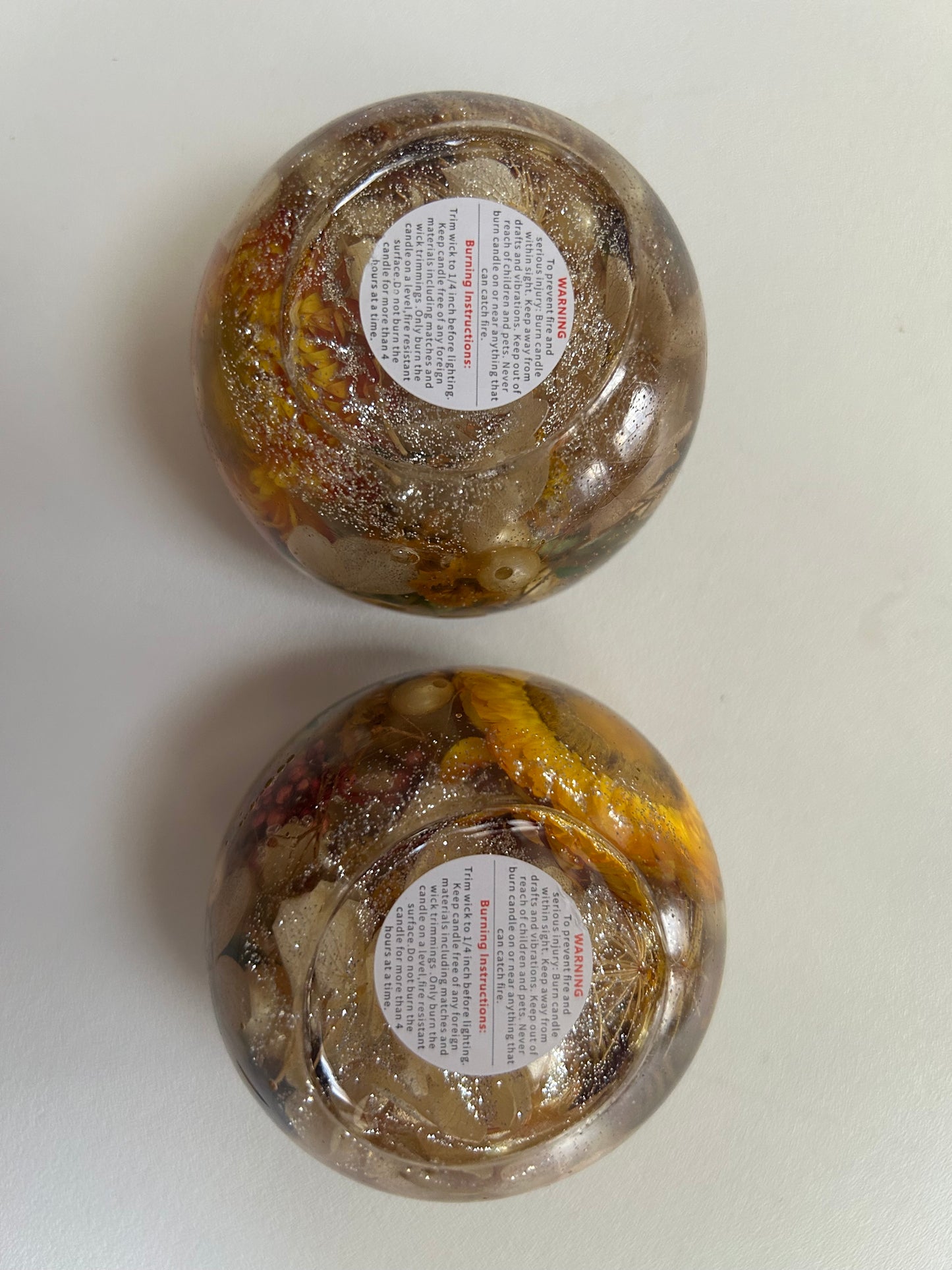 Two glass jars with decorative contents and labels on a white background