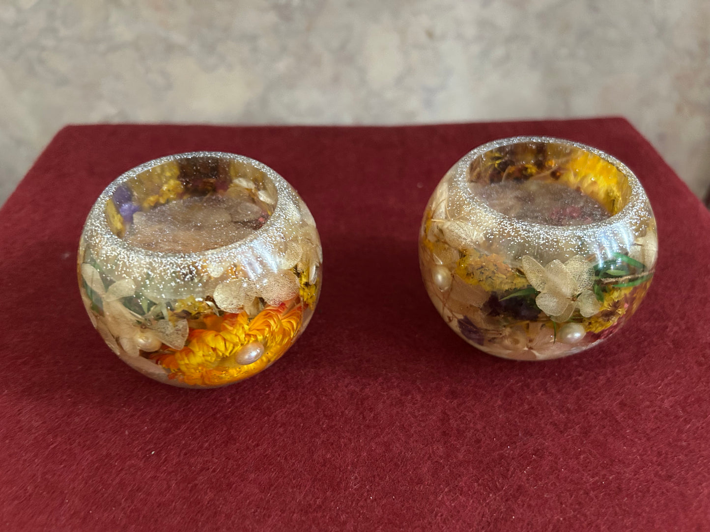 Two decorative glass containers with floral designs on a red surface.