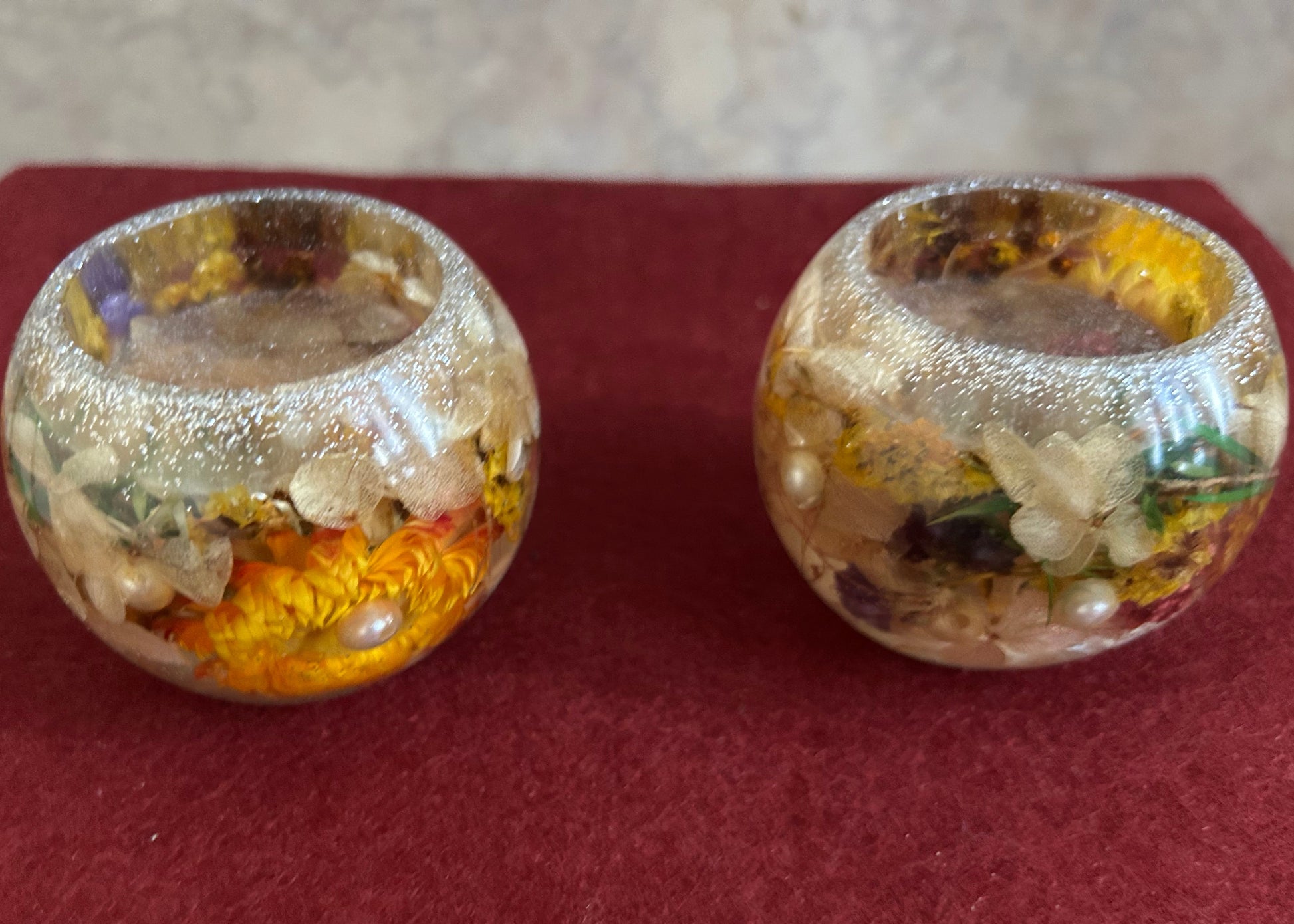 Two decorative glass containers with floral and pearl elements on a red surface.