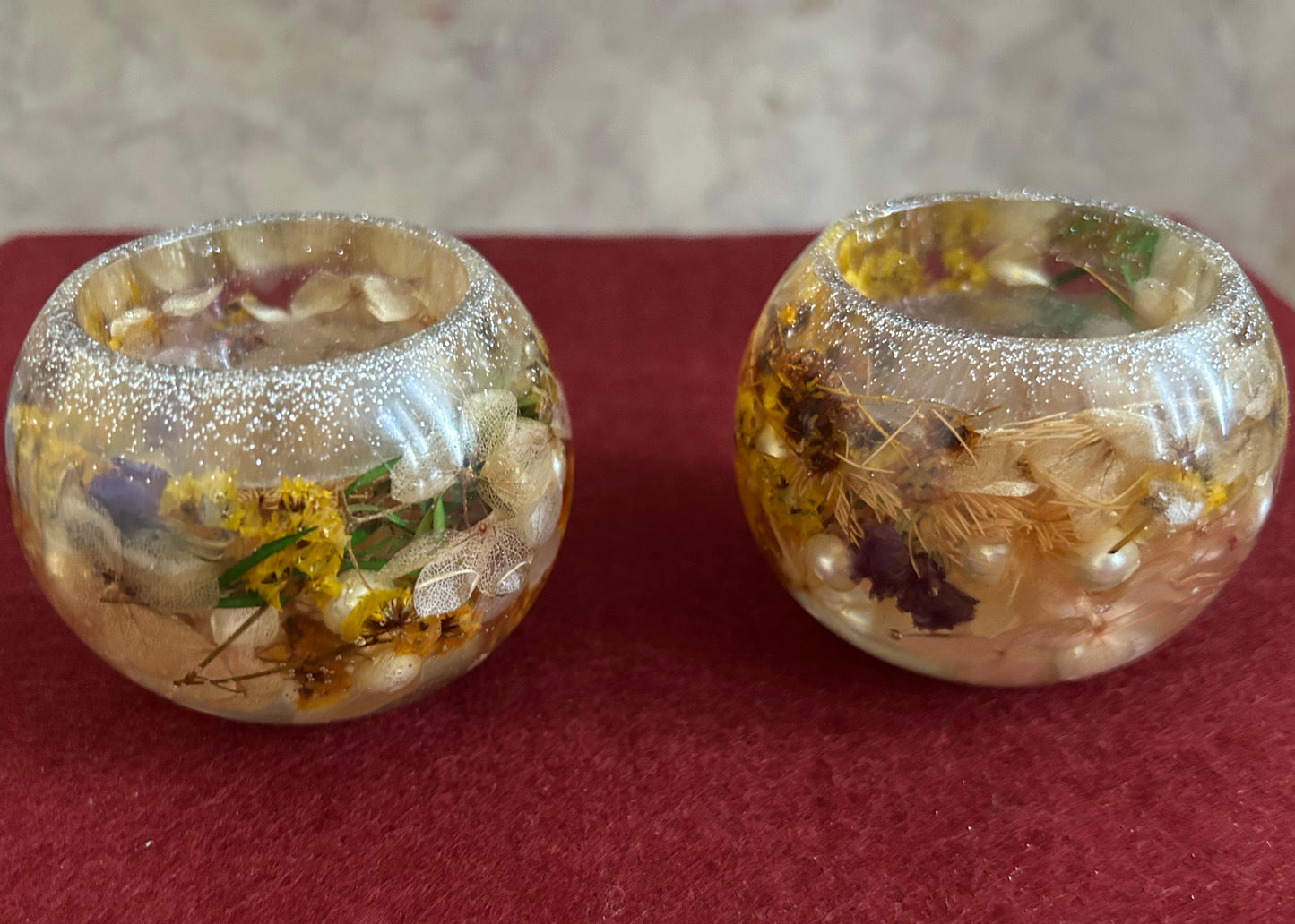 Two decorative glass containers with embedded flowers and pearls on a red surface.